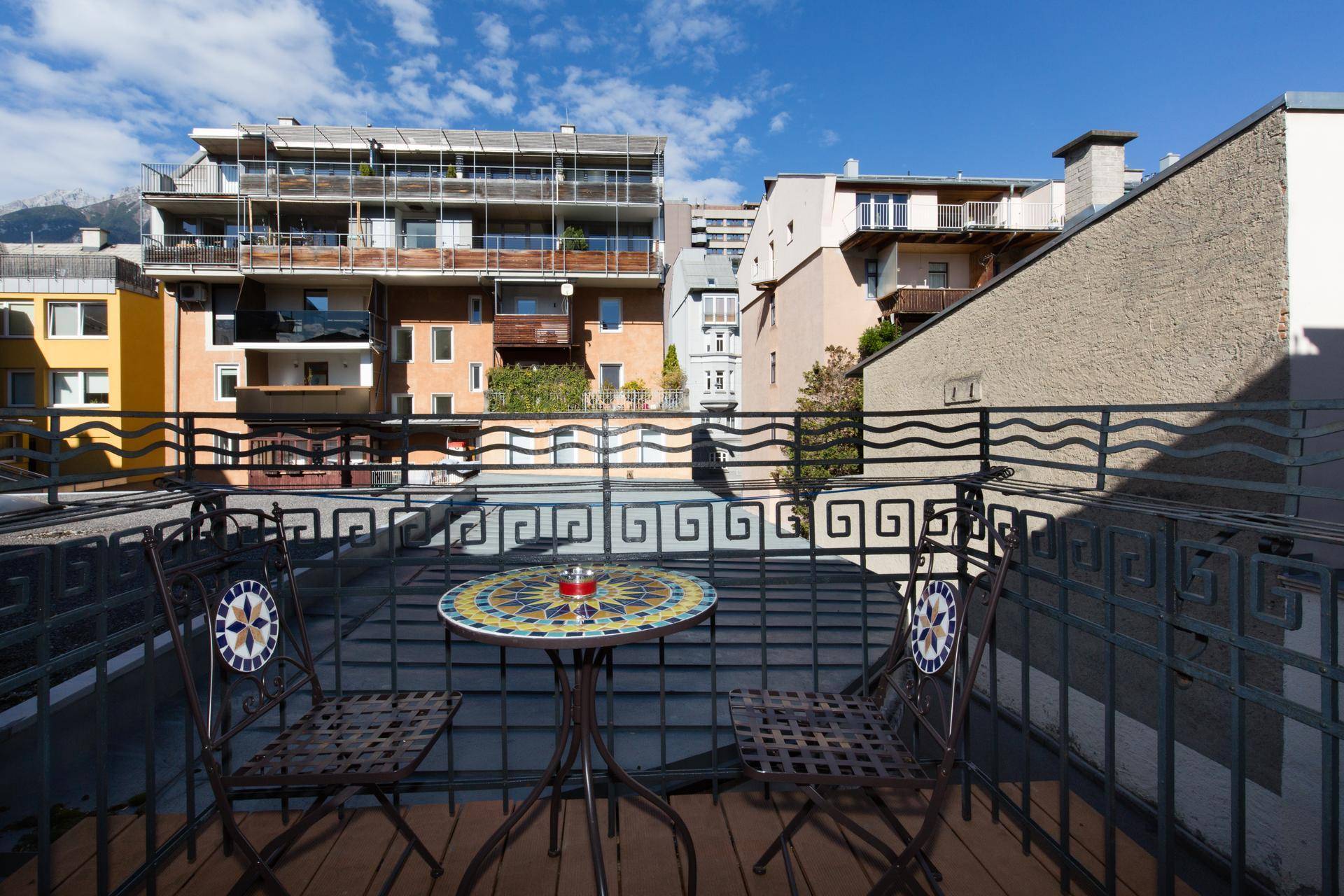 Kleiner Balkon mit schmiedeeisernen Möbeln und Blick auf umliegende Gebäude und Berge.