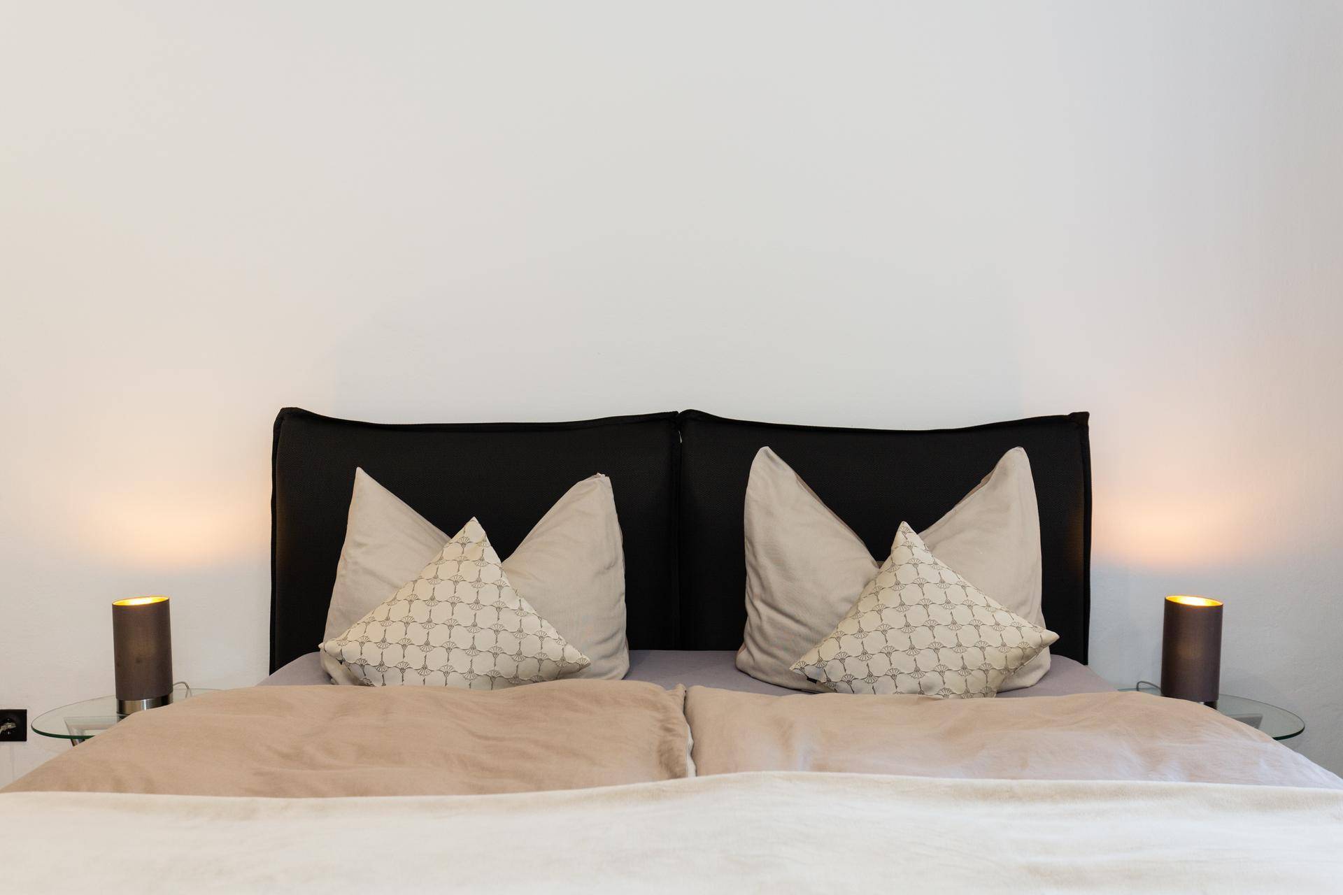 Nahaufnahme eines gemütlichen Bettes mit beigen Kissen und Nachttischlampen in einem Schlafzimmer.