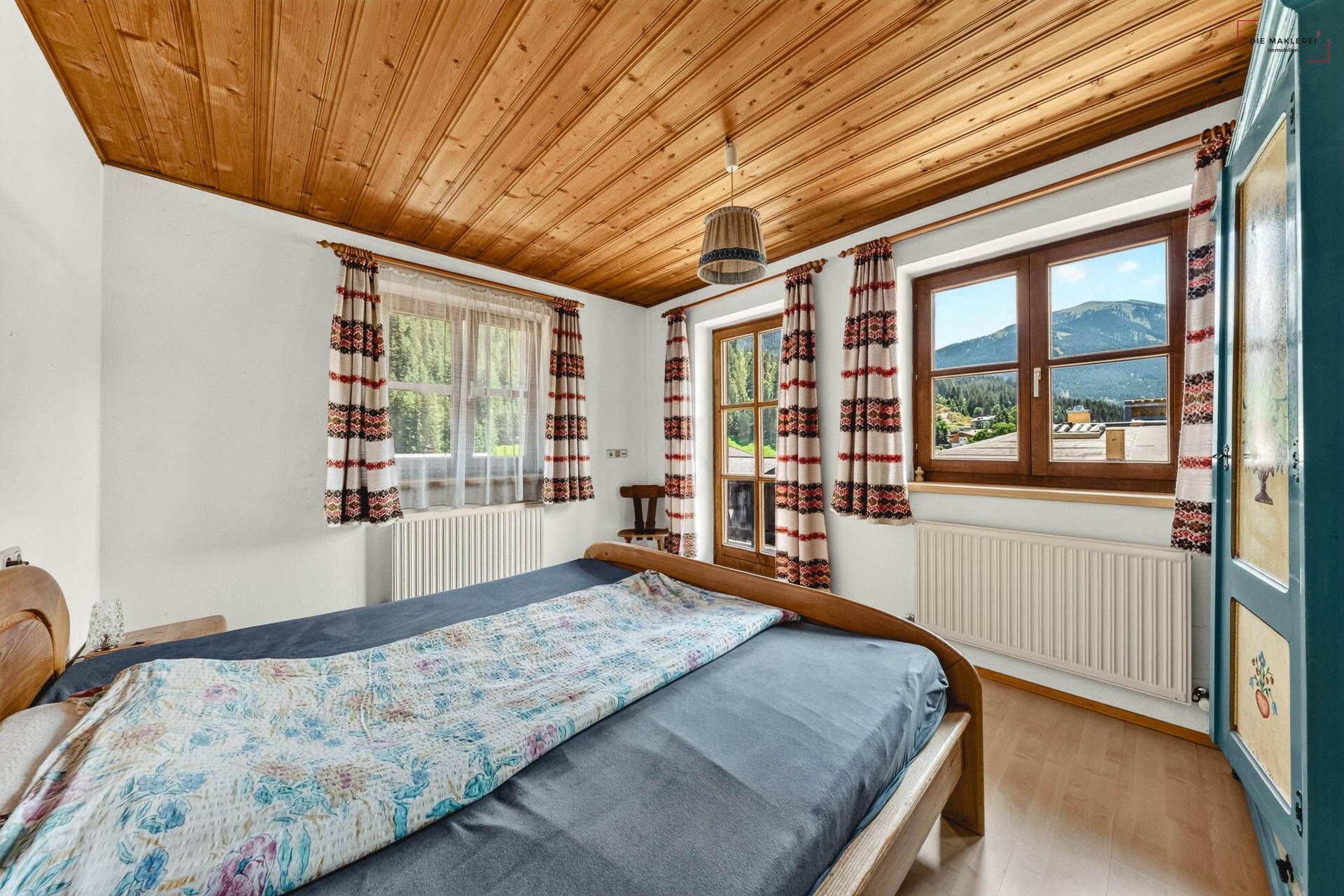Helles Schlafzimmer mit Holzboden, Holzdecke und Bergblick aus den Fenstern.