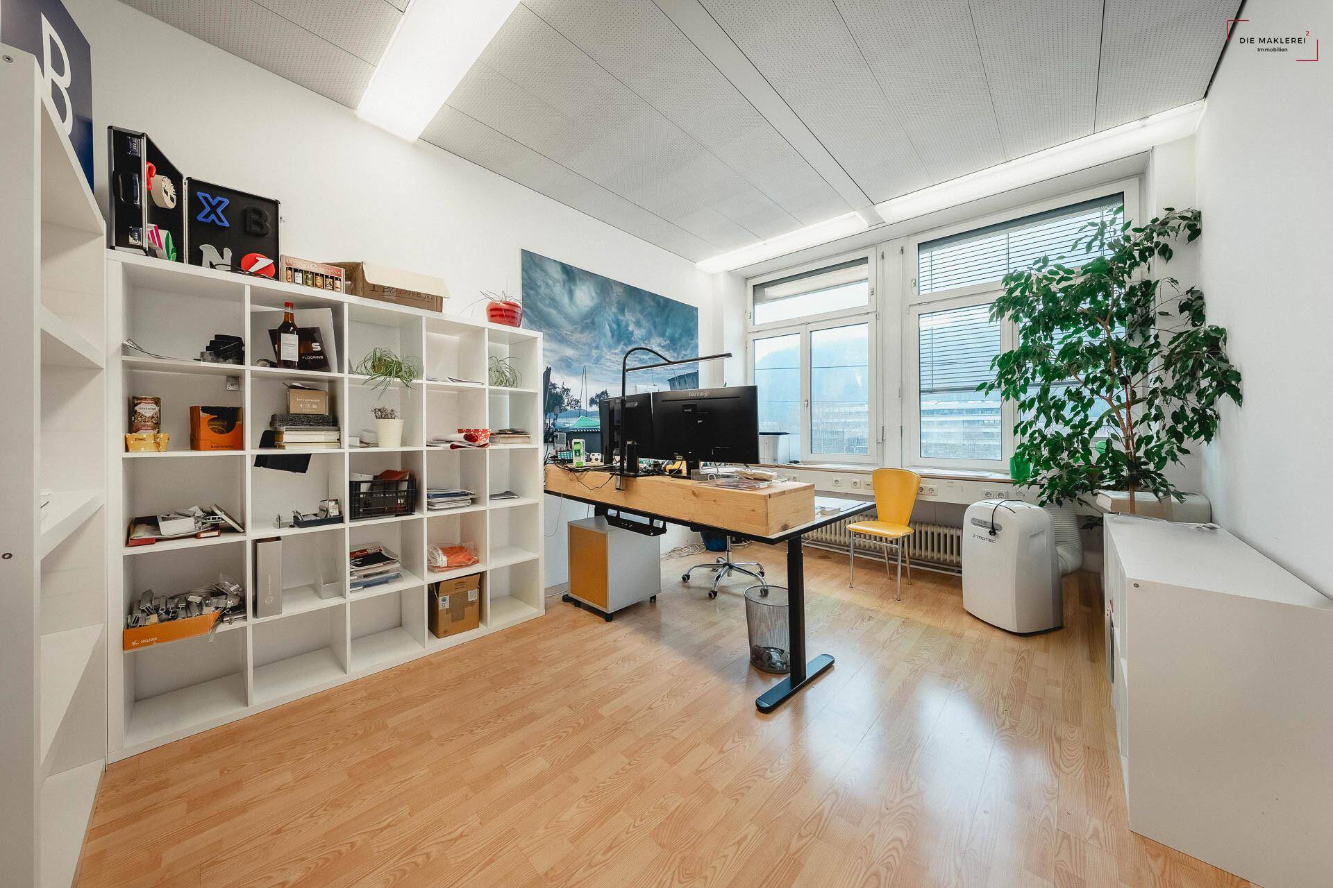 Helles Büro mit weißen Regalen, Laminatboden und einem großen Fenster mit Jalousien für Privatsphäre.