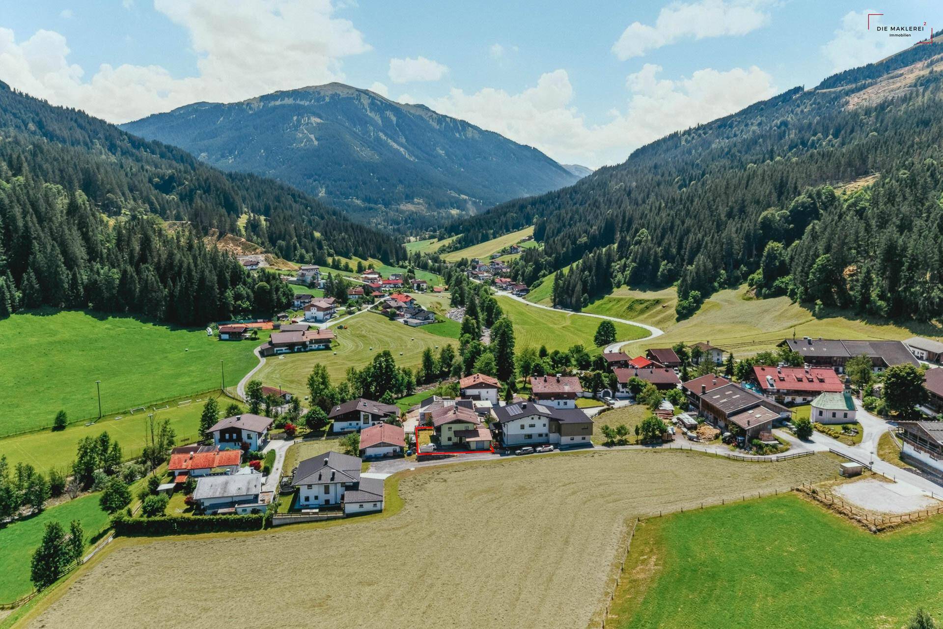 Luftaufnahme eines malerischen Dorfes eingebettet in ein grünes Tal mit majestätischen Bergen.