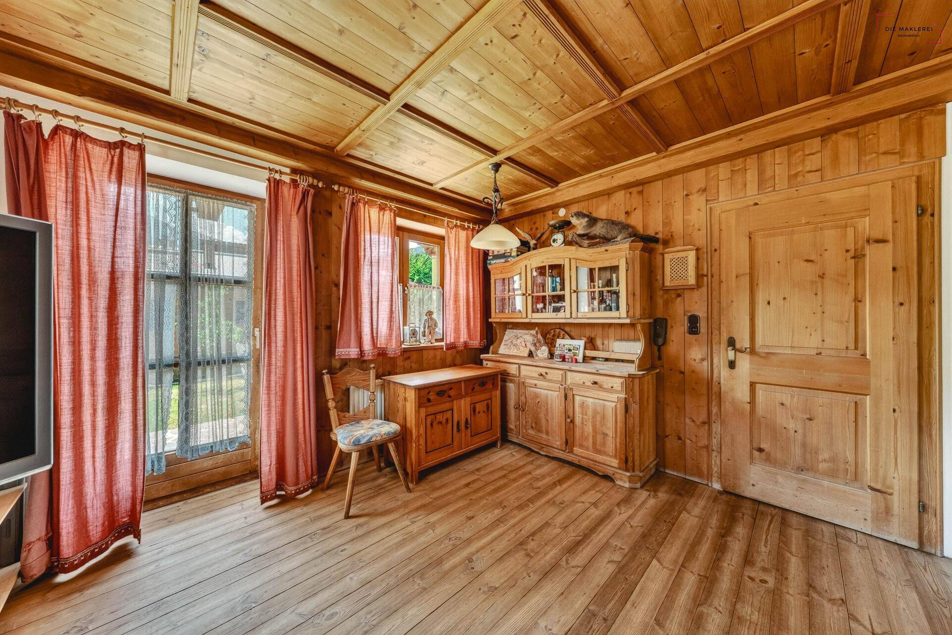 Rustikales Wohnzimmer mit Holzwänden, Holzdecke und Zugang zum Gartenbereich durch eine Glastür.