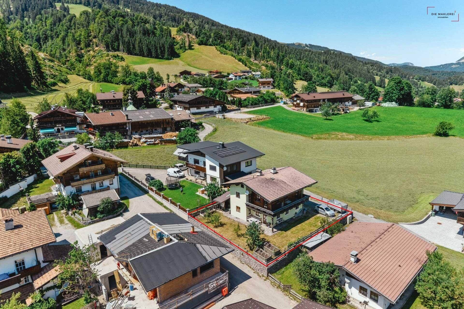 Detaillierte Luftaufnahme eines charmanten Chalets mit Garten und Parkplatz in alpiner Umgebung.