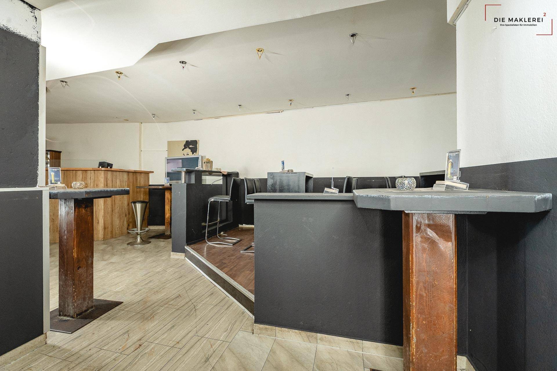 Sitzbereich der Bar mit dunklen Tischen und Stühlen auf einer erhöhten Plattform und gefliestem Boden.