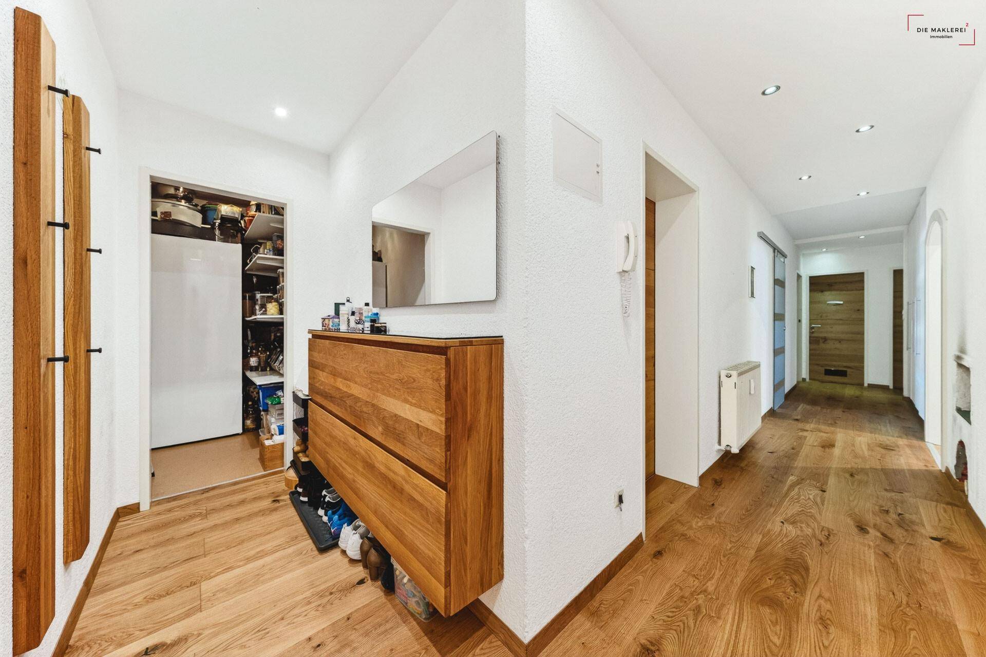 Heller Flur mit Holzboden, modernem Schuhschrank und Spiegel.