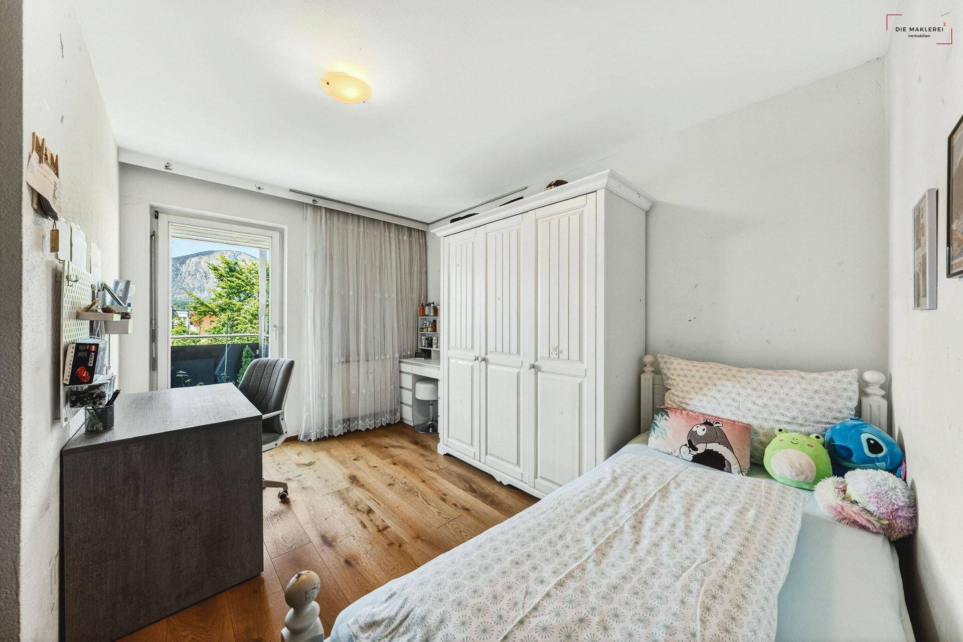 Kinderzimmer mit Schreibtisch, weißem Kleiderschrank und Zugang zum Balkon.