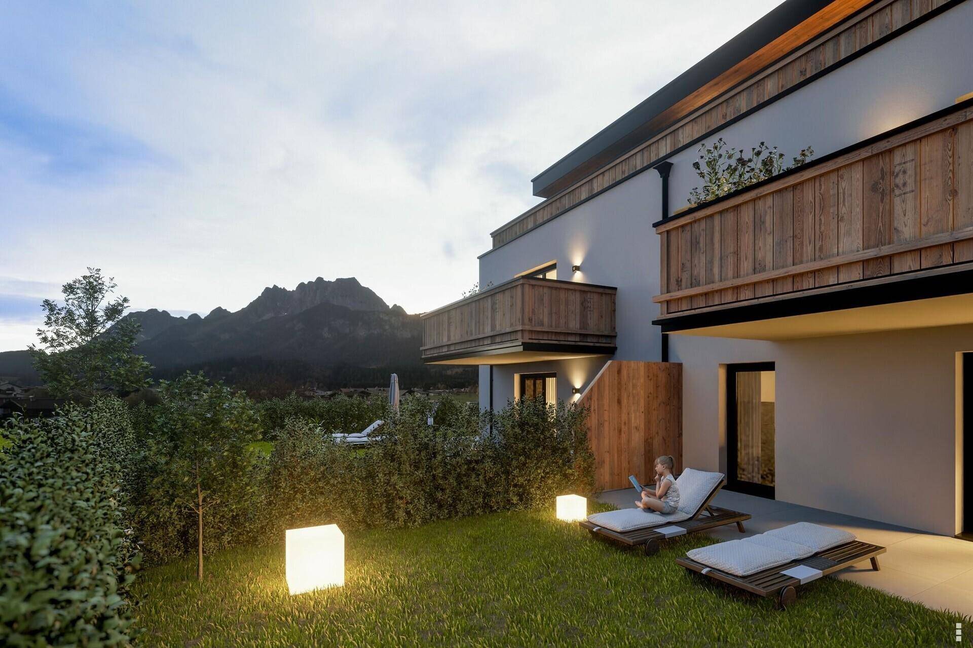 Abendliche Ansicht eines modernen Wohnhauses mit beleuchtetem Gartenbereich und Bergblick.