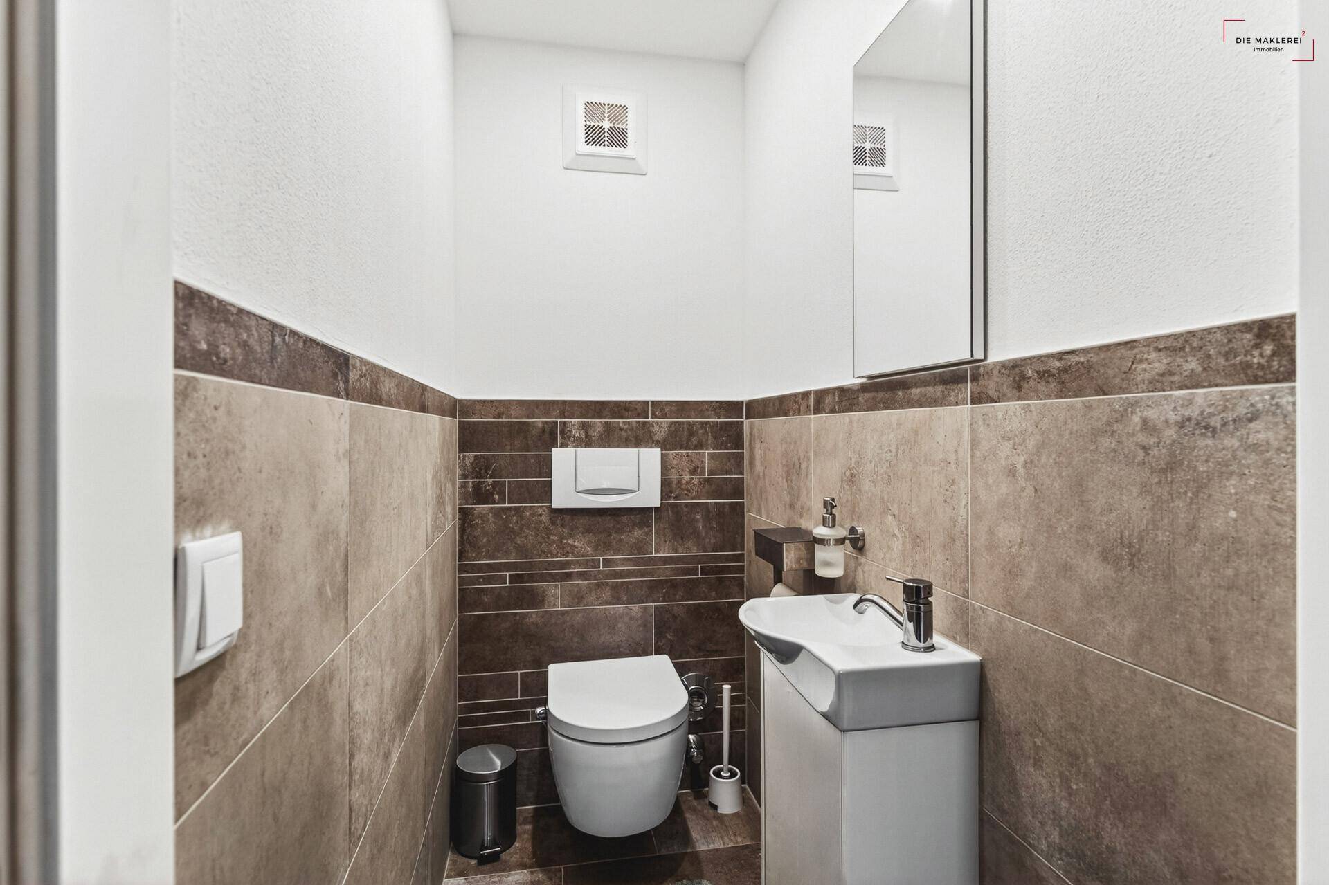 Kleines Gäste-WC mit Wand-WC, Waschbecken und modernen Fliesen.
