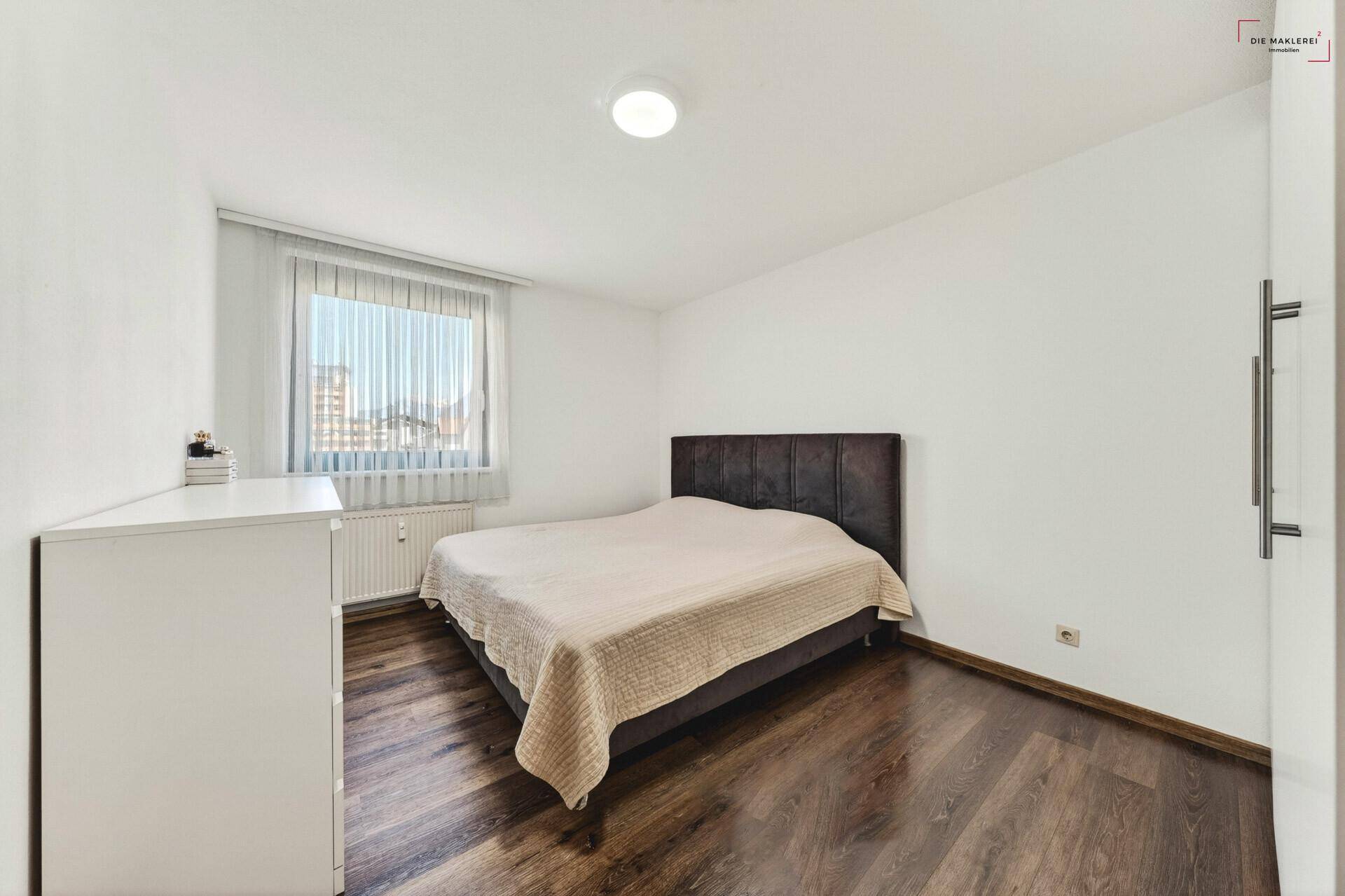 Schlafzimmer mit Doppelbett, Kommode und Holzboden, hell und schlicht eingerichtet.