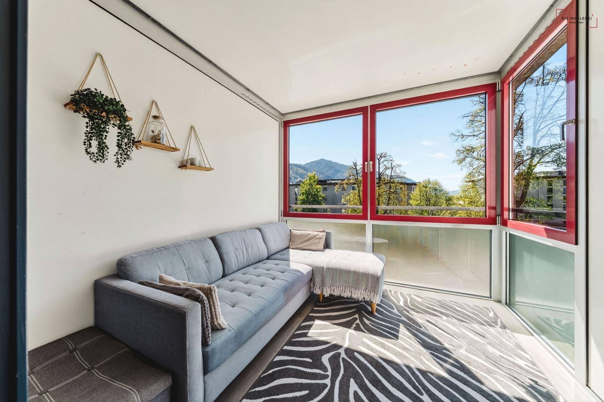 Gemütliche Loggia mit Sofa und großen Fenstern, bietet einen schönen Blick ins Grüne und auf die Berge.