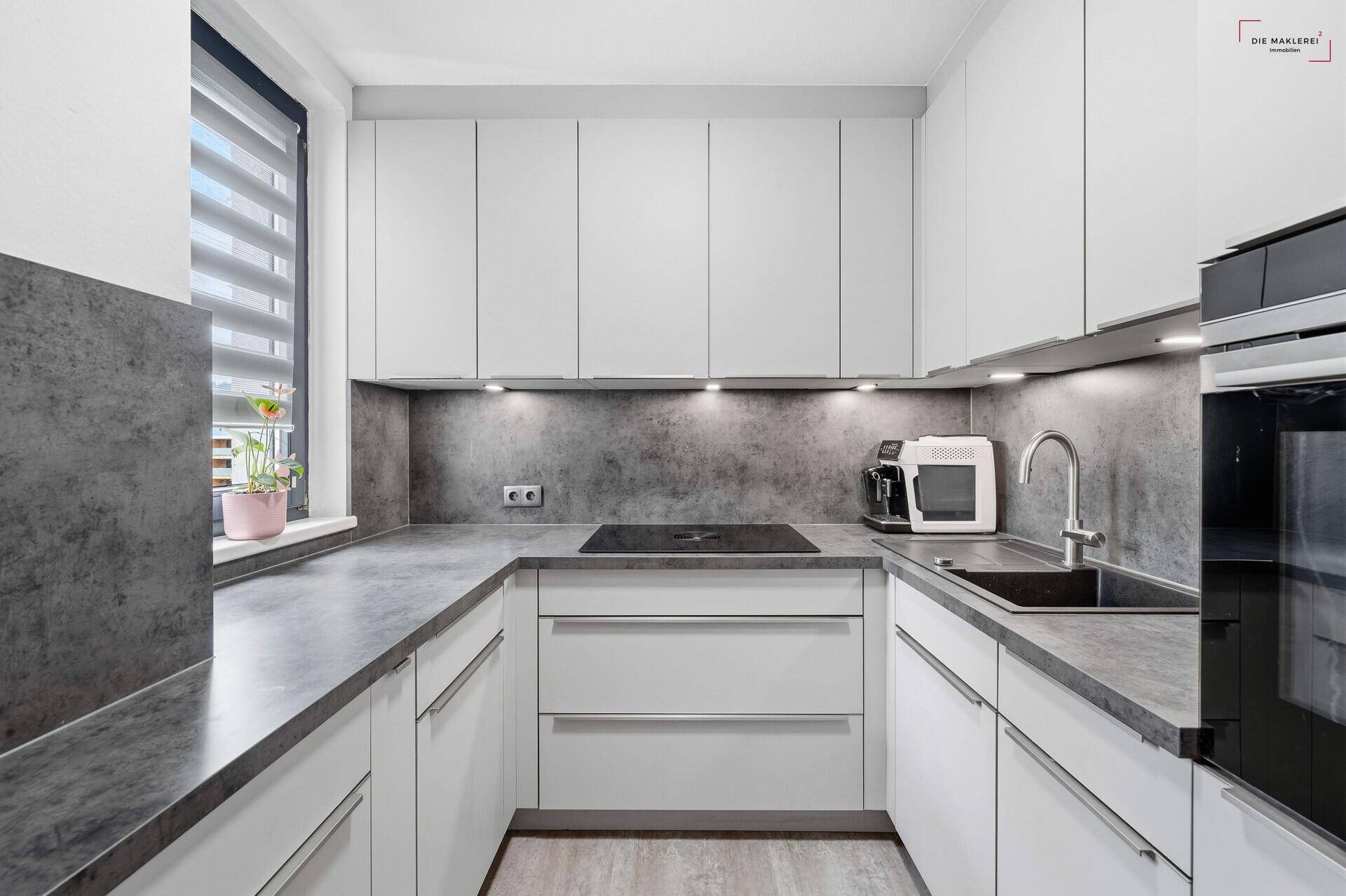 Moderne Einbauküche mit weißen Schränken, dunkler Arbeitsplatte und Induktionskochfeld.