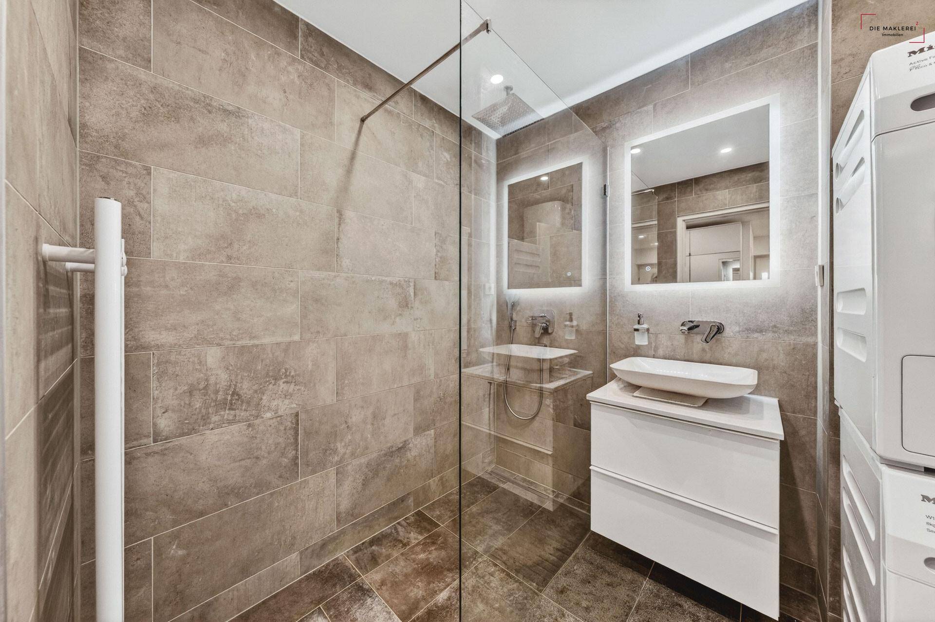 Modernes Badezimmer mit begehbarer Dusche, beleuchtetem Spiegel und Waschmaschine.