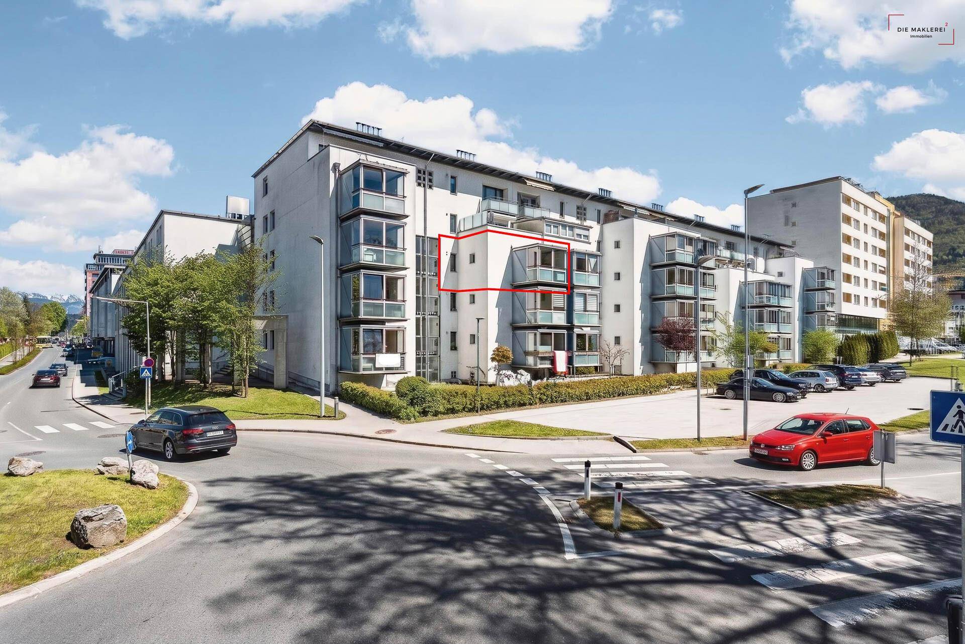 Modernes Mehrfamilienhaus mit mehreren Balkonen und umliegenden Parkplätzen in städtischer Umgebung.