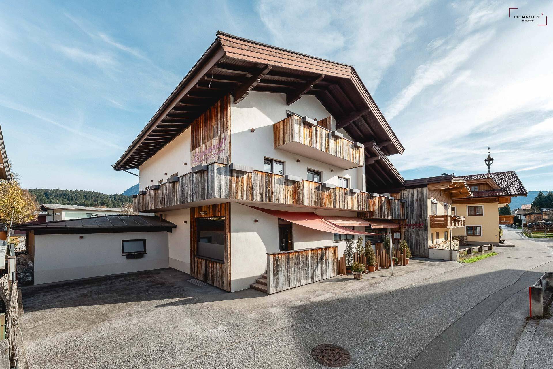 Ansicht des Gebäudes mit Holzverkleidung und Balkonen, umgeben von einer ländlichen Umgebung unter klarem Himmel.