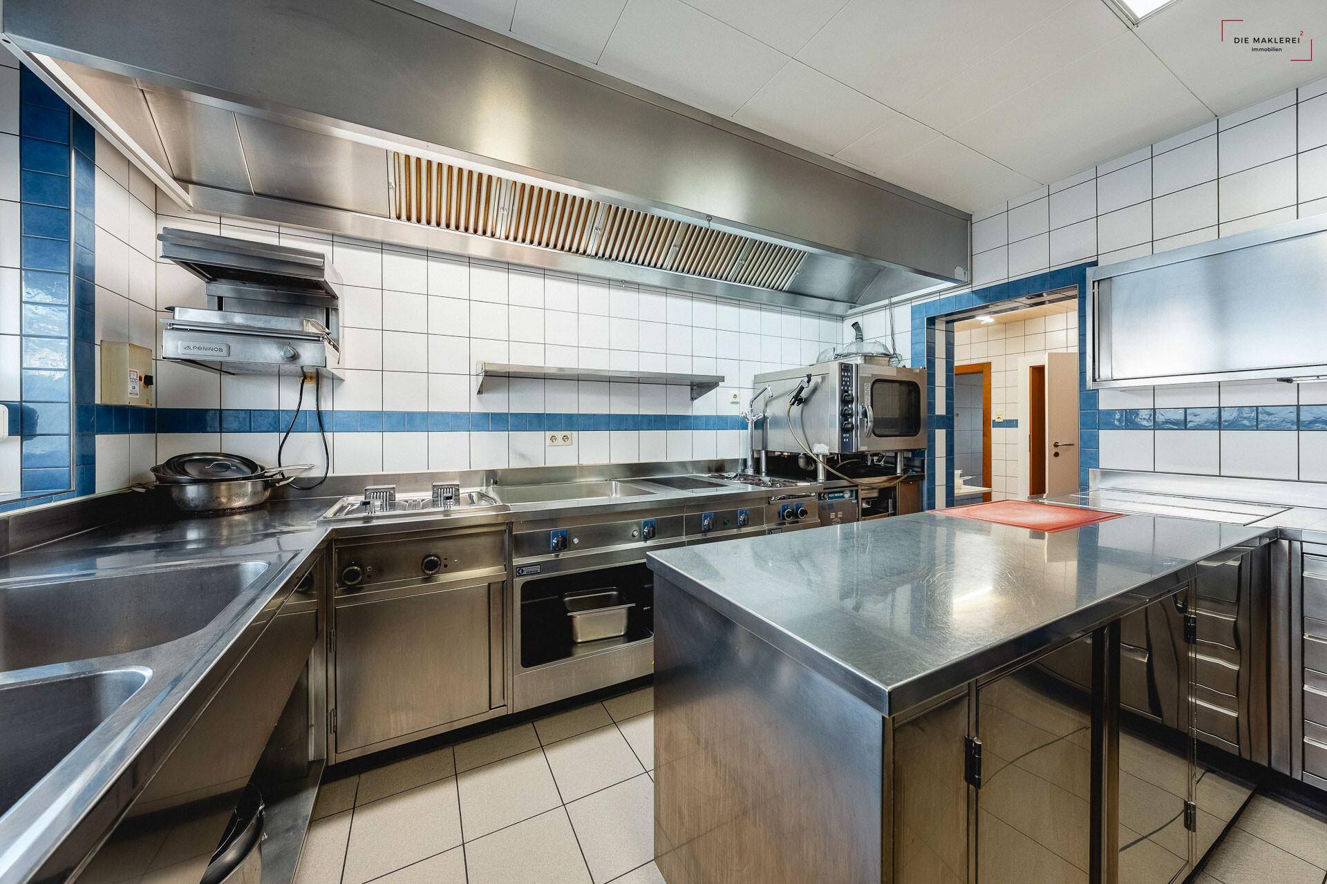 Gut ausgestattete Gewerbeküche mit mehreren Kochstationen, Edelstahlmöbeln und Fliesenboden.