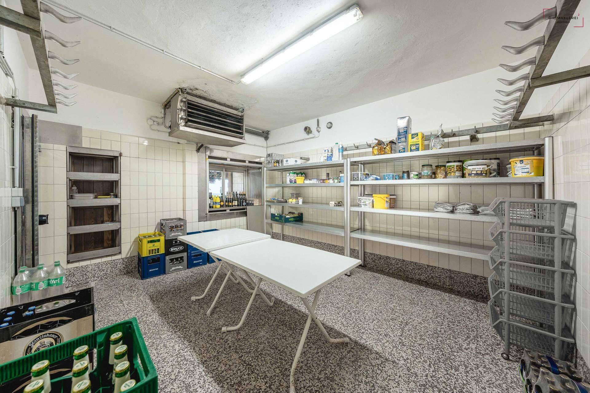 Geräumiger Lagerraum mit Fliesenwänden, Regalen und einem Kühlsystem an der Decke.