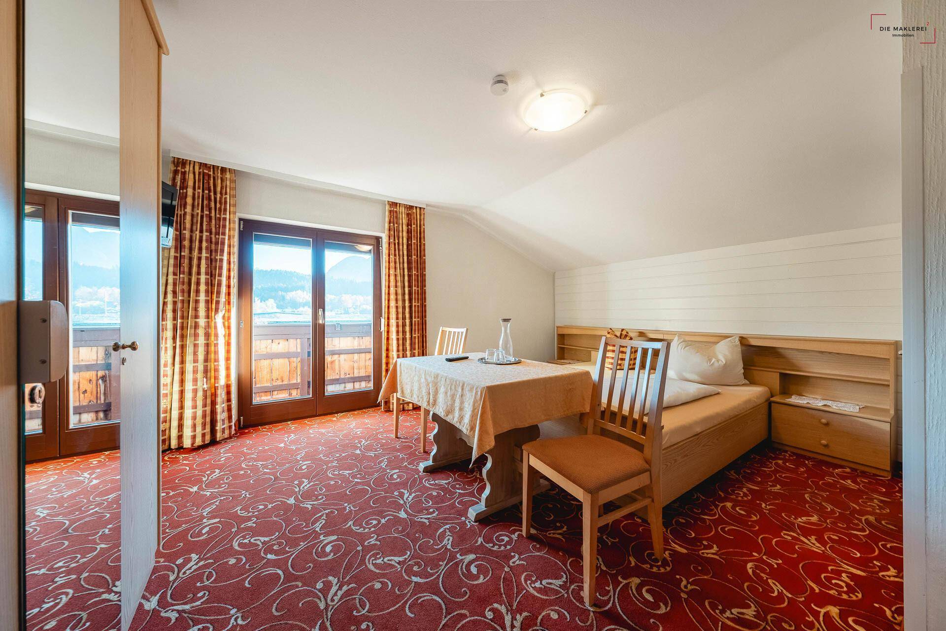 Gemütliches Schlafzimmer mit Teppichboden, Einzelbett und Zugang zu einem Balkon mit Bergblick.
