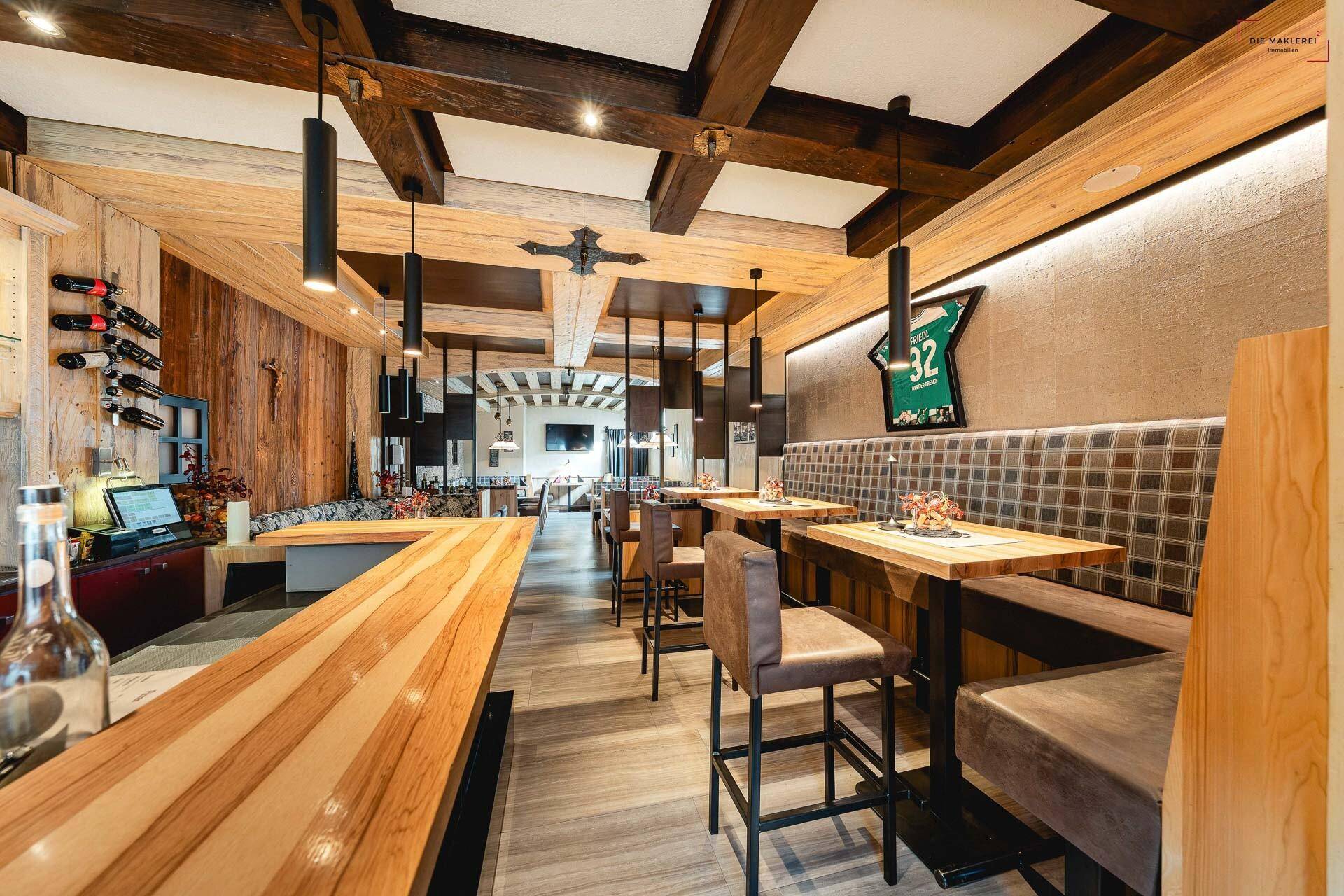 Modernes Restaurant mit Holzbalkendecke, gepolsterten Sitzbänken und einer Bar im Vordergrund.