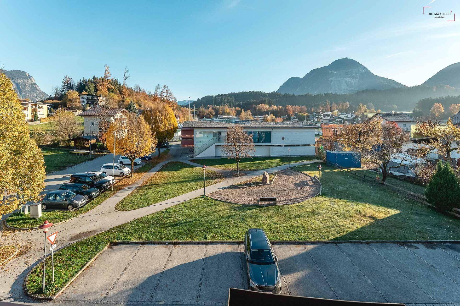Weitläufiger Ausblick auf die Berglandschaft, umliegende Gebäude und einen Parkplatz unter blauem Himmel.