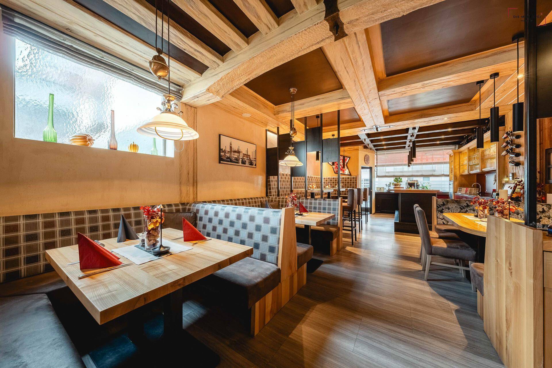 Helles Restaurant mit großen Fenstern, Holzbalken und einer Mischung aus modernen und traditionellen Elementen.
