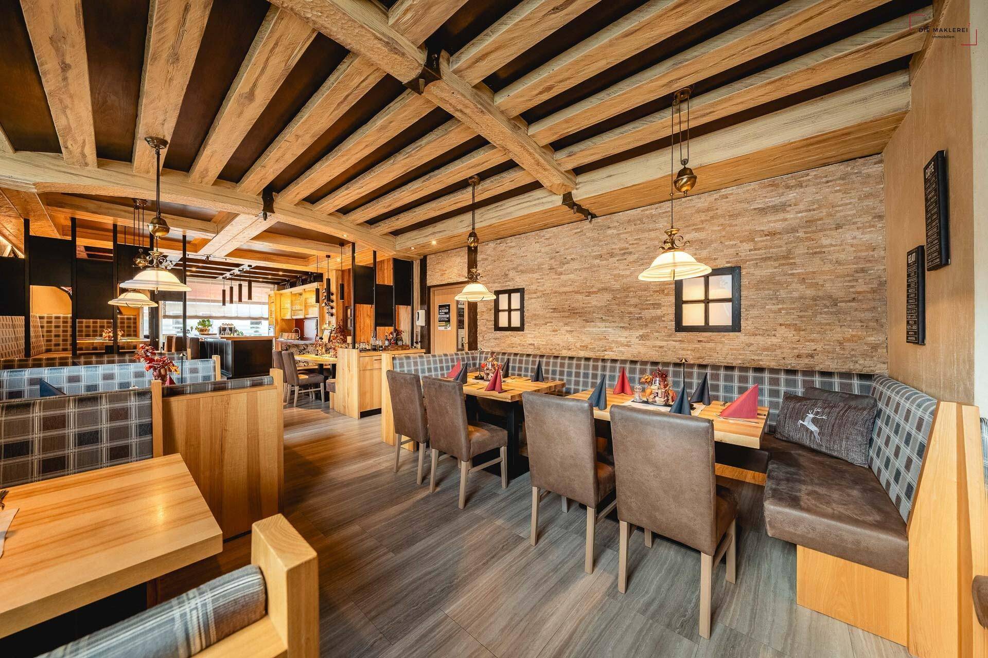Traditioneller Restaurantbereich mit Holzbalken, Steinwand und bequemen Sitzbänken für Gäste.