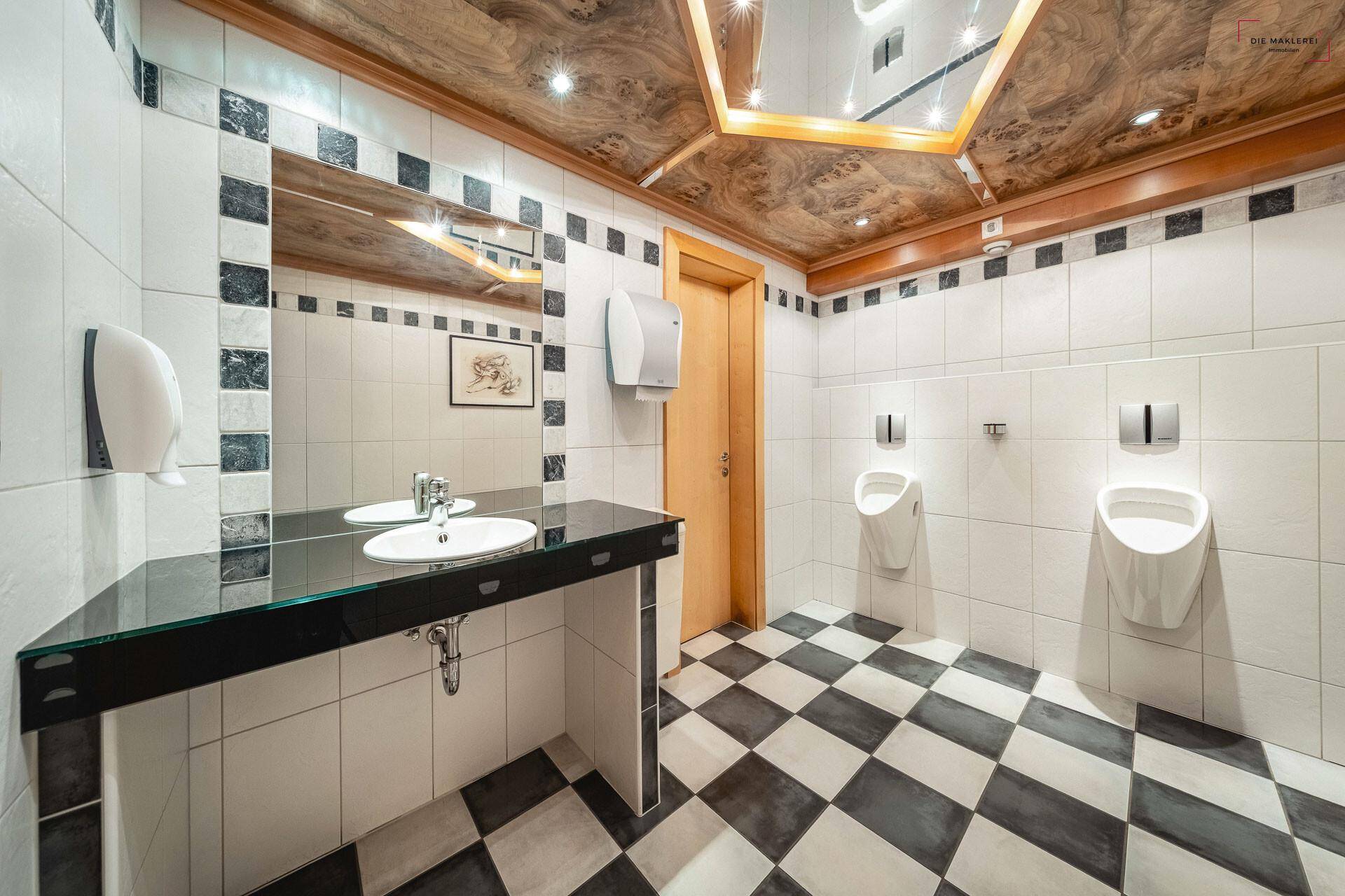 Moderne Herrentoilette mit schwarz-weißem Schachbrettmuster auf dem Boden und zwei Urinalen.