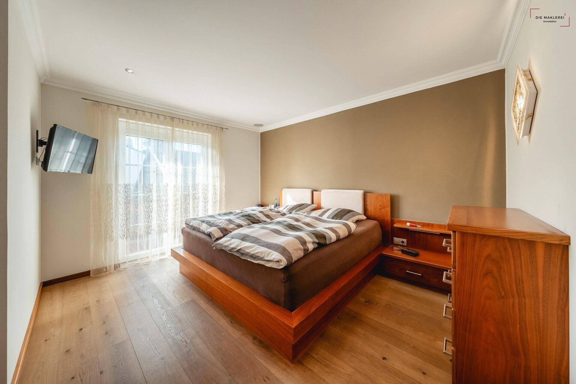 Gemütliches Schlafzimmer mit großem Doppelbett, Holzmöbeln und einem Fenster mit Vorhängen.