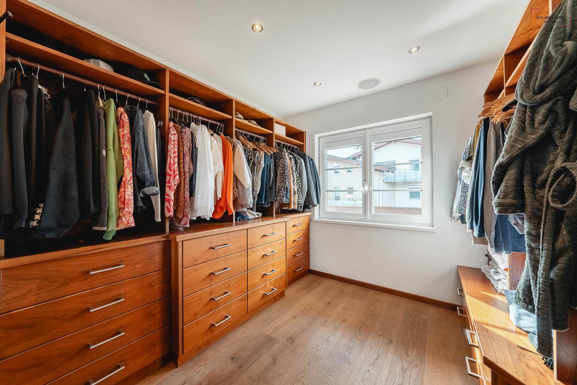 Geräumiger begehbarer Kleiderschrank mit maßgefertigten Holzschränken und viel Stauraum.