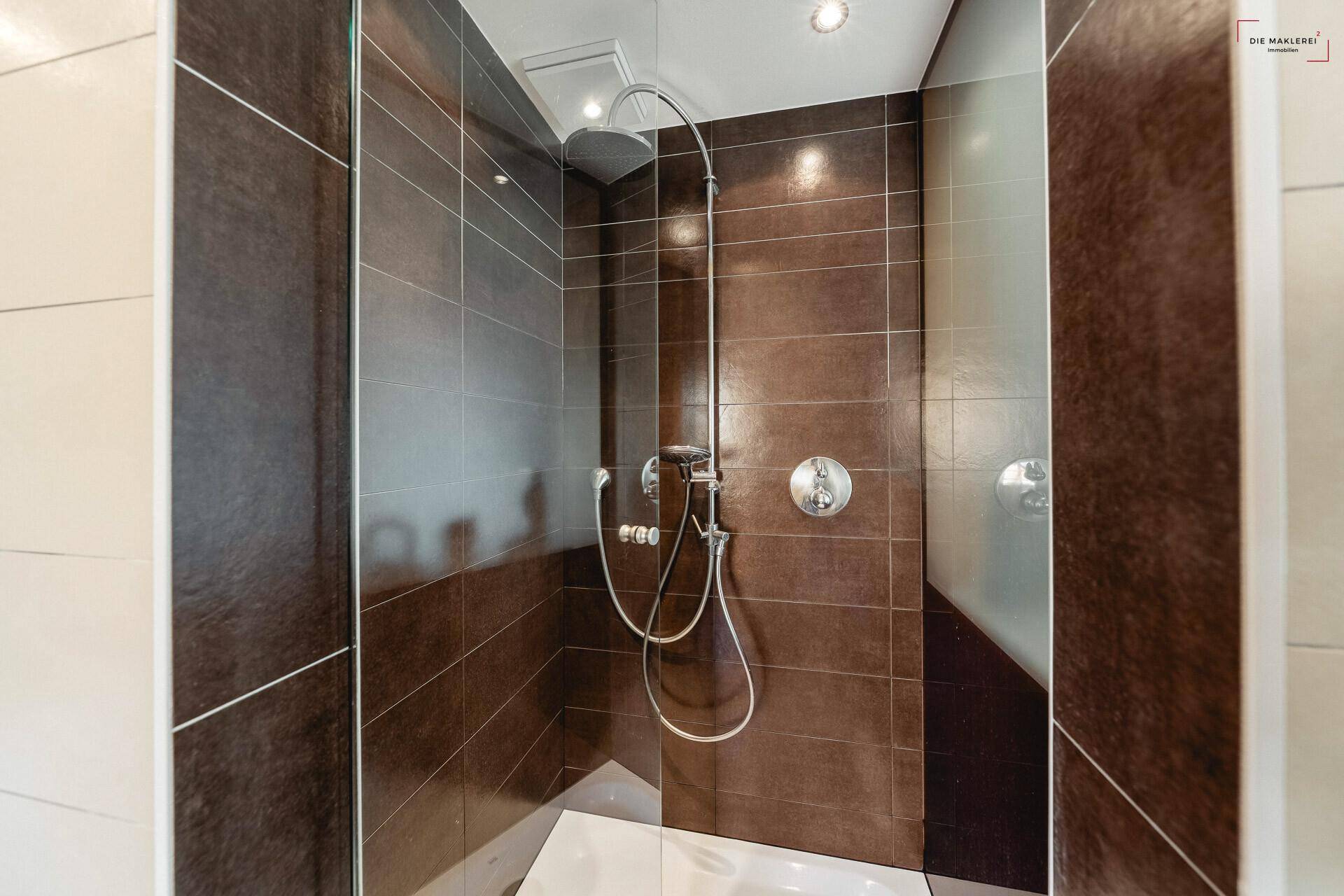 Moderne Duschkabine mit dunkelbraunen Fliesen und einer luxuriösen Regendusche.