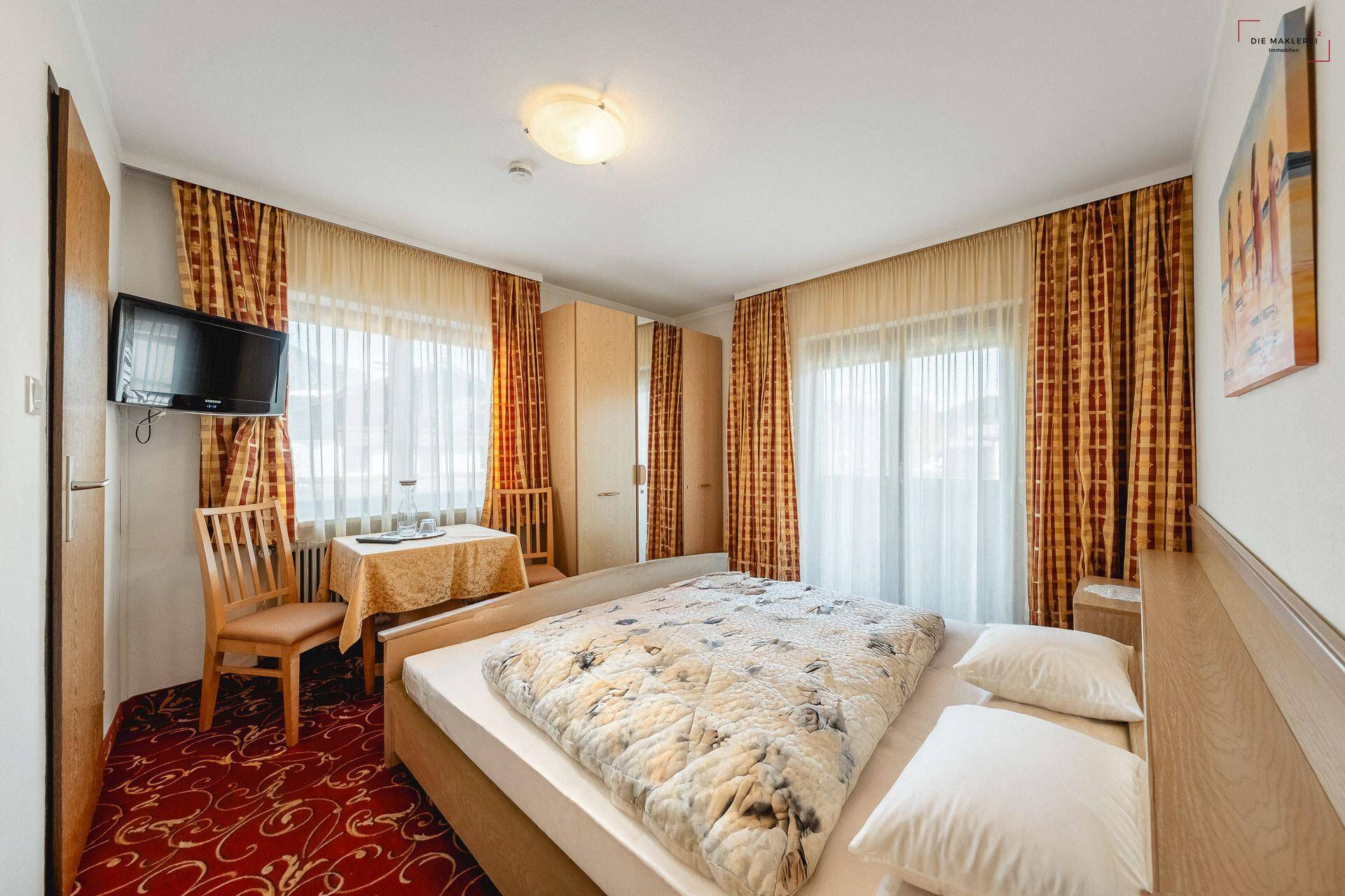 Gemütliches Schlafzimmer mit Doppelbett, kleinem Tisch und farbenfrohen Vorhängen.
