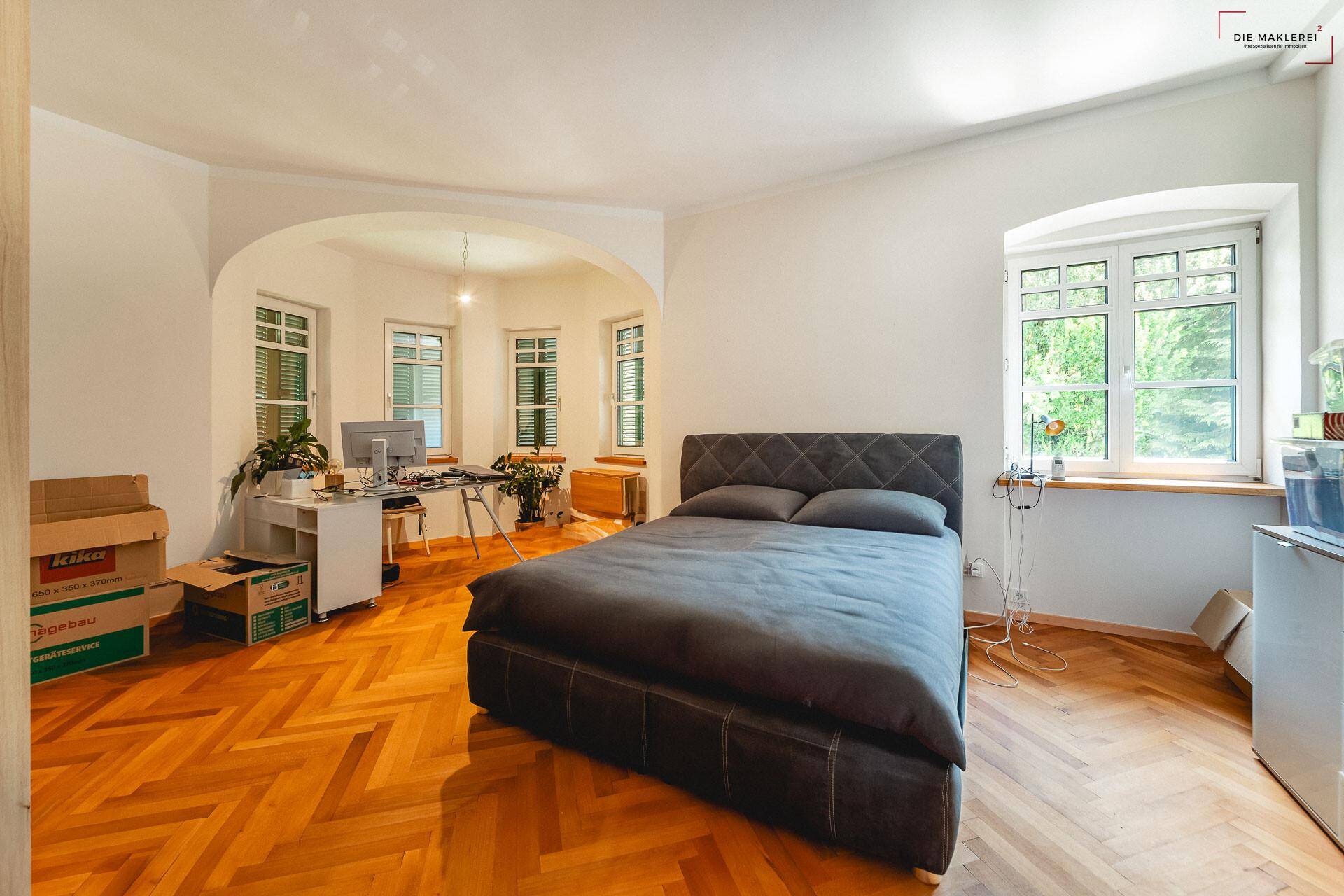 Geräumiges Schlafzimmer mit Fischgrätparkett und einem hellen Arbeitsbereich im Erker.