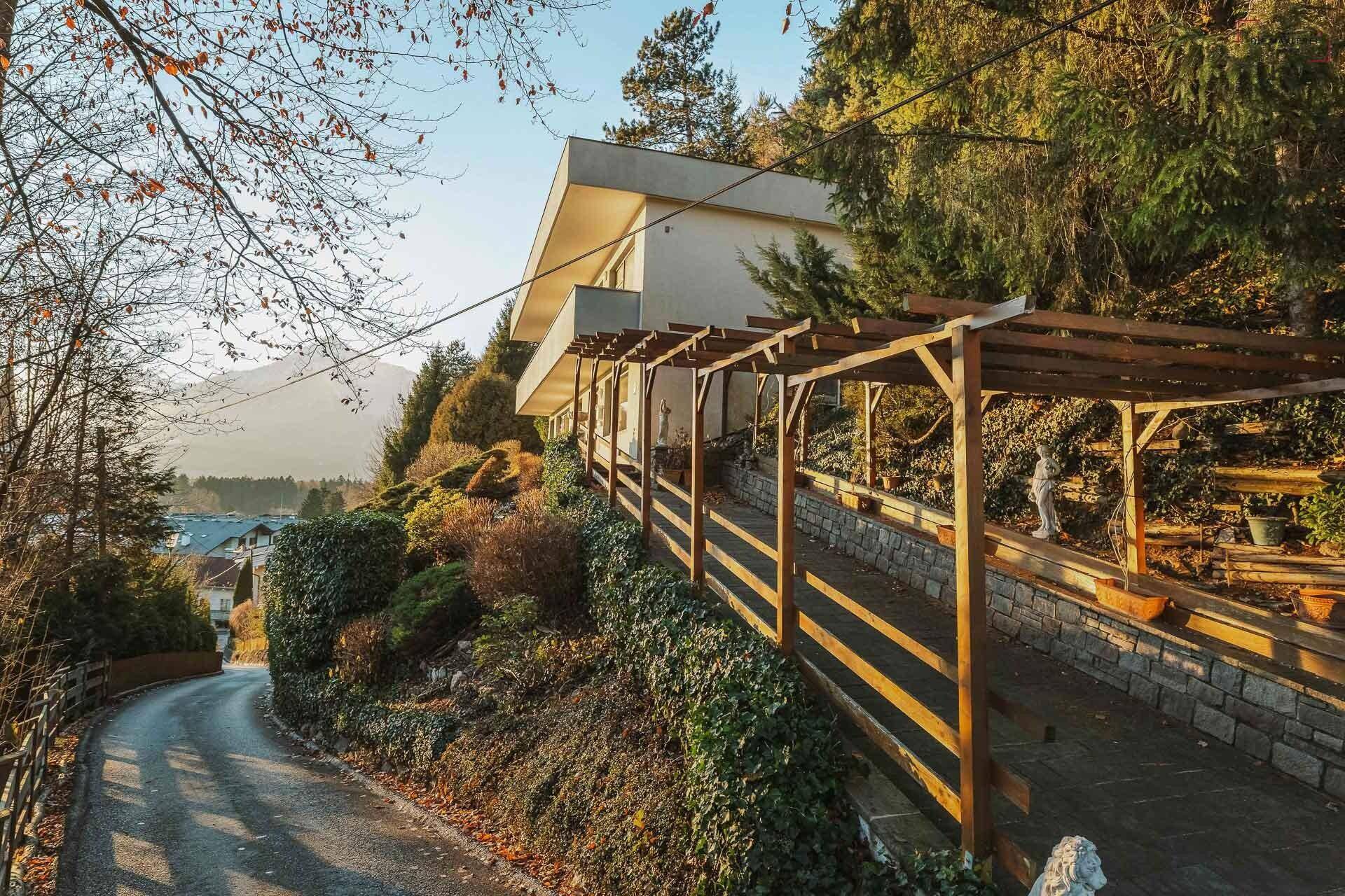Zufahrt zum Anwesen mit einer Holzpergola und einer gepflegten Bepflanzung am Hang.