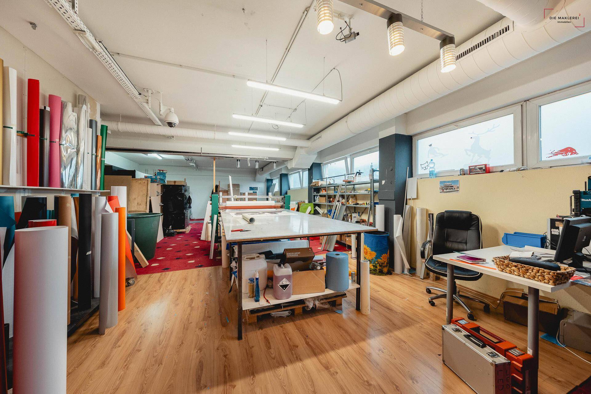 Großer Werkstattraum mit Laminatboden, Arbeitstischen und großen Fenstern, ideal für handwerkliche Tätigkeiten.