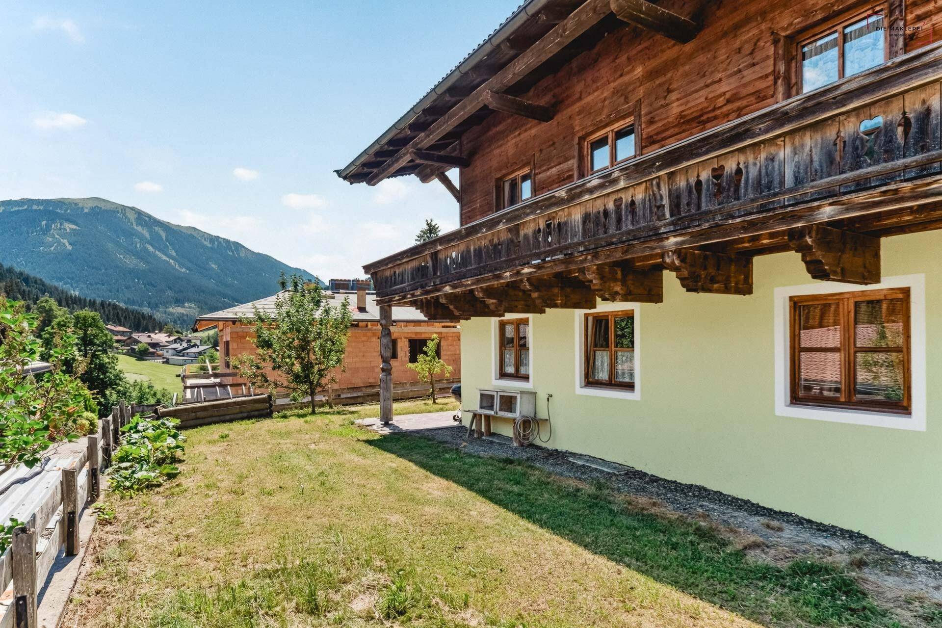 Seitenansicht des Hauses mit Rasenfläche, jungen Bäumen und Bergblick im Hintergrund.