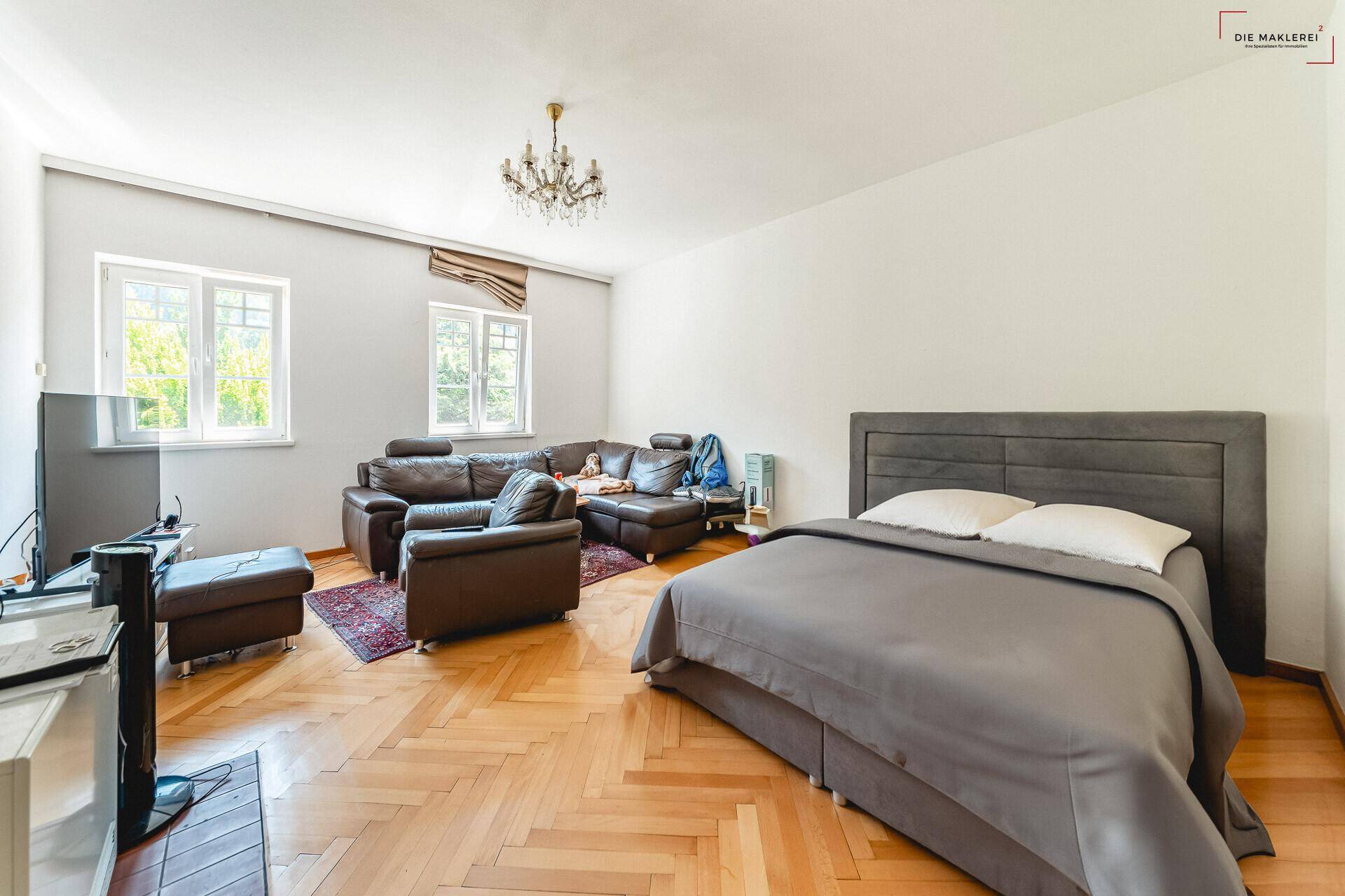 Großzügiges Schlafzimmer mit Fischgrätparkett, bequemer Sitzecke und viel Tageslicht.
