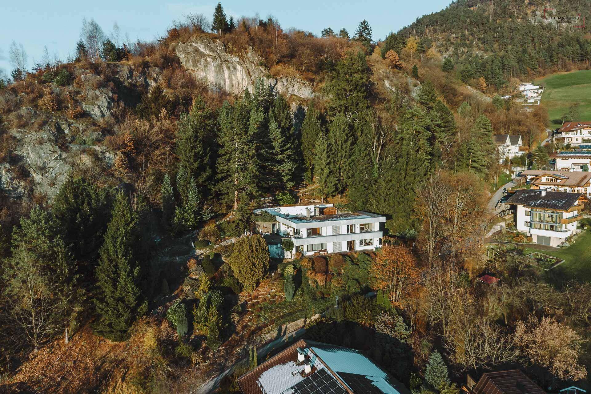 Luftaufnahme des modernen Hauses auf einem bewaldeten Hügel mit markierter Grundstücksgrenze und Bergblick.