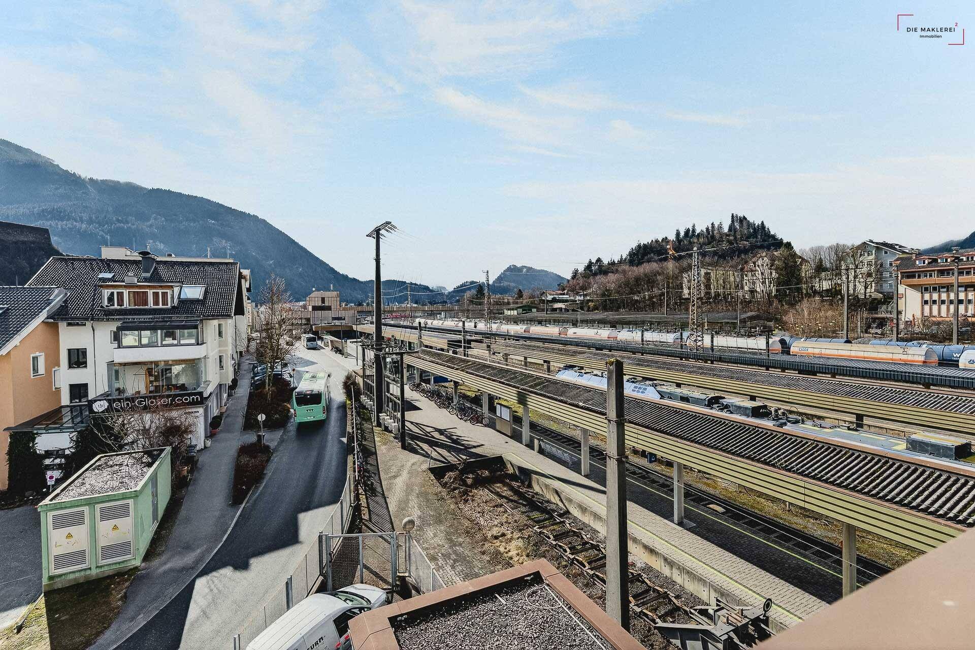 Panoramablick über eine Straße, den Bahnhof und die bergige Landschaft unter blauem Himmel.