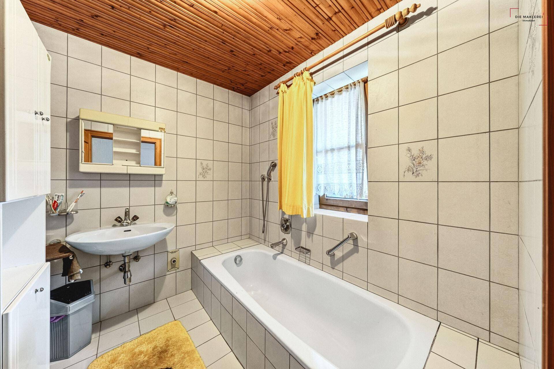 Gefliestes Badezimmer mit Badewanne, Waschbecken, Spiegelschrank und Holzdecke.