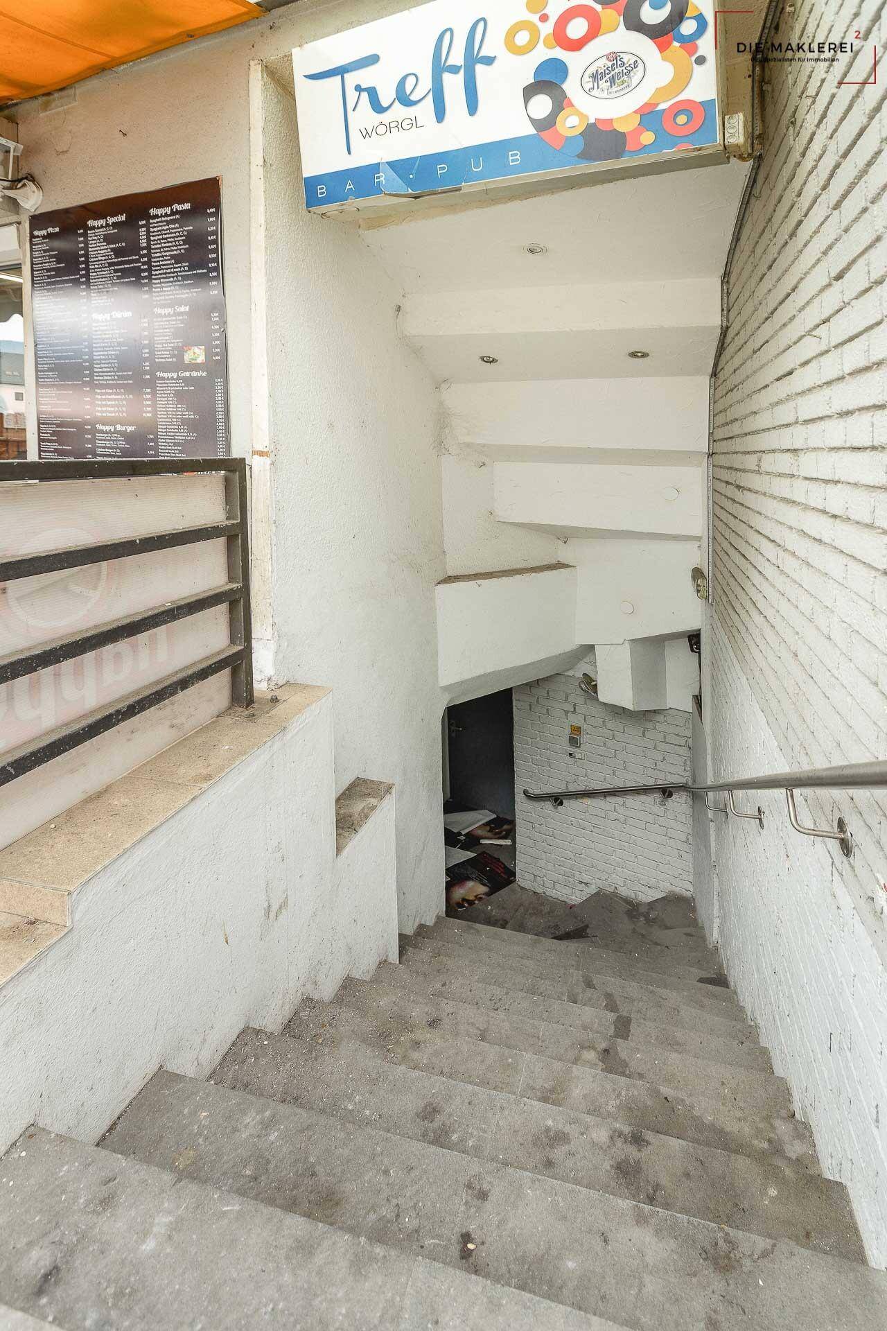 Eingangsbereich mit Treppe, die zu einem Bar/Pub führt, mit einem Schild "Treff Wörgl".