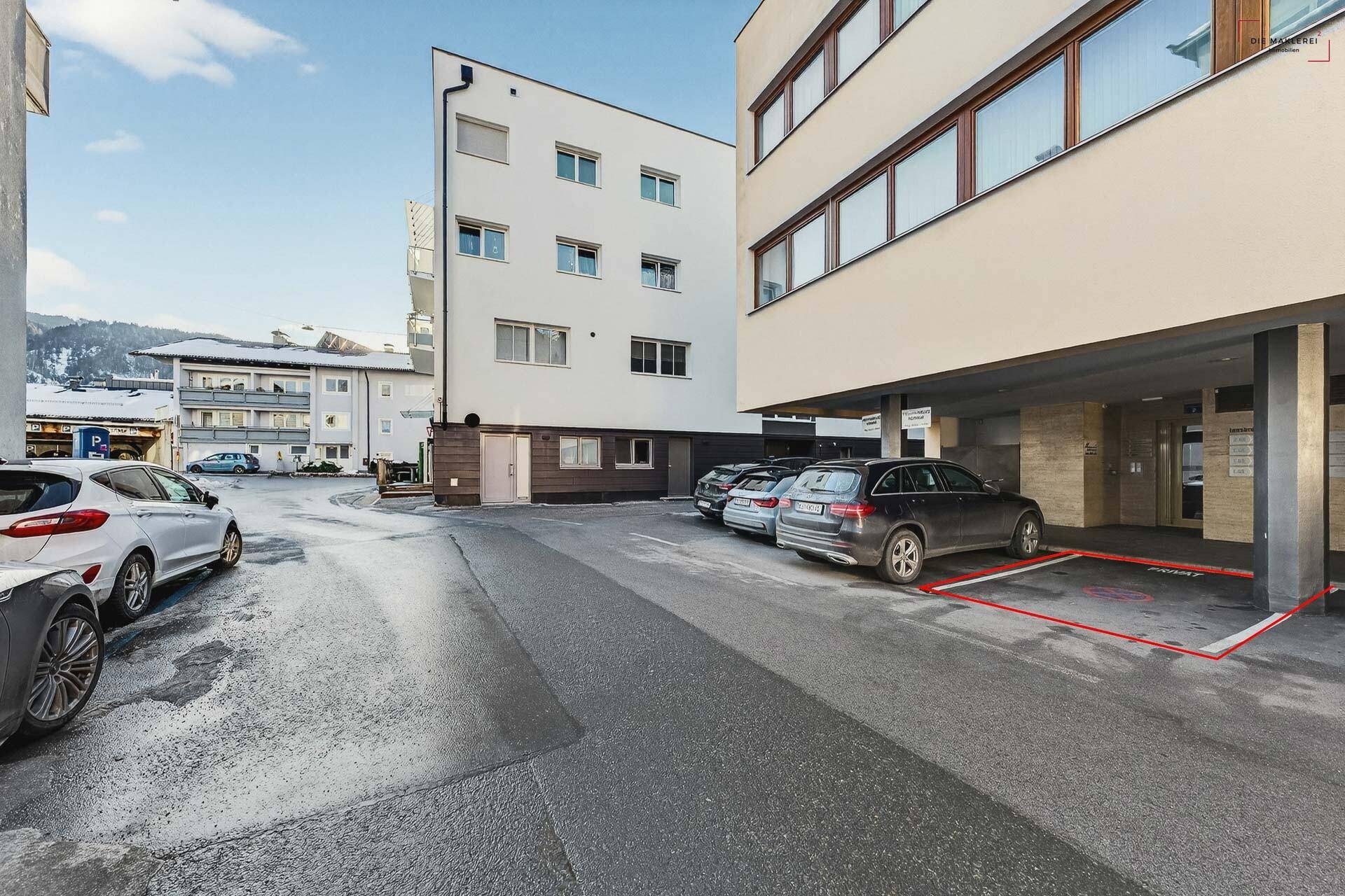 Außenansicht des modernen Gebäudes mit Parkplätzen und einer Tiefgarageneinfahrt im Vordergrund.