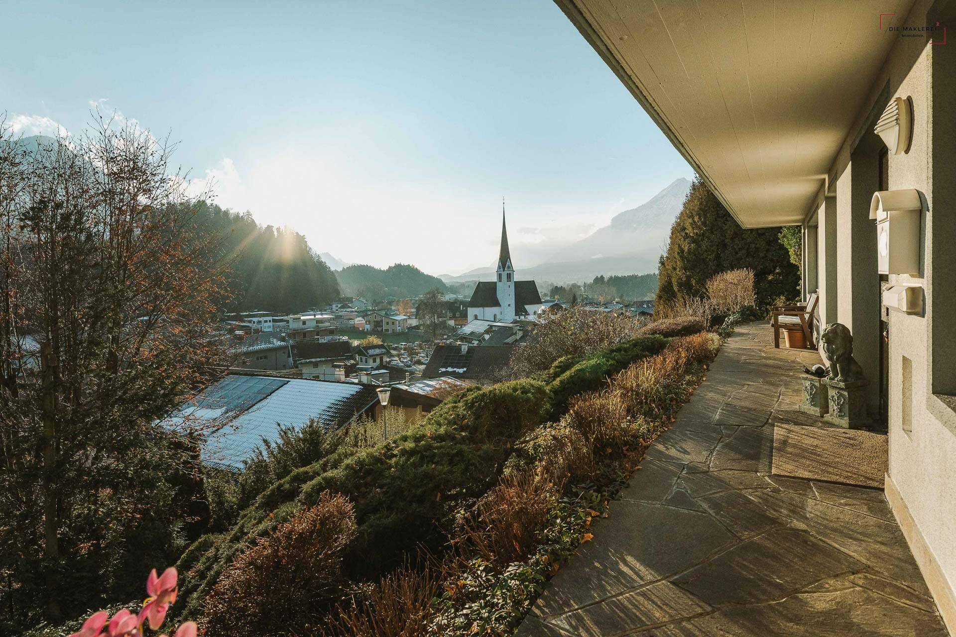 Überdachte Veranda mit Steinboden und einem malerischen Blick auf die Kirche und die Berglandschaft.