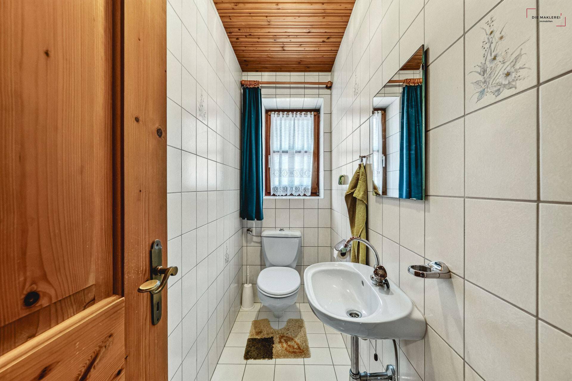 Kleines Gäste-WC mit Fliesen, Waschbecken, Toilette und Fenster mit Vorhang.