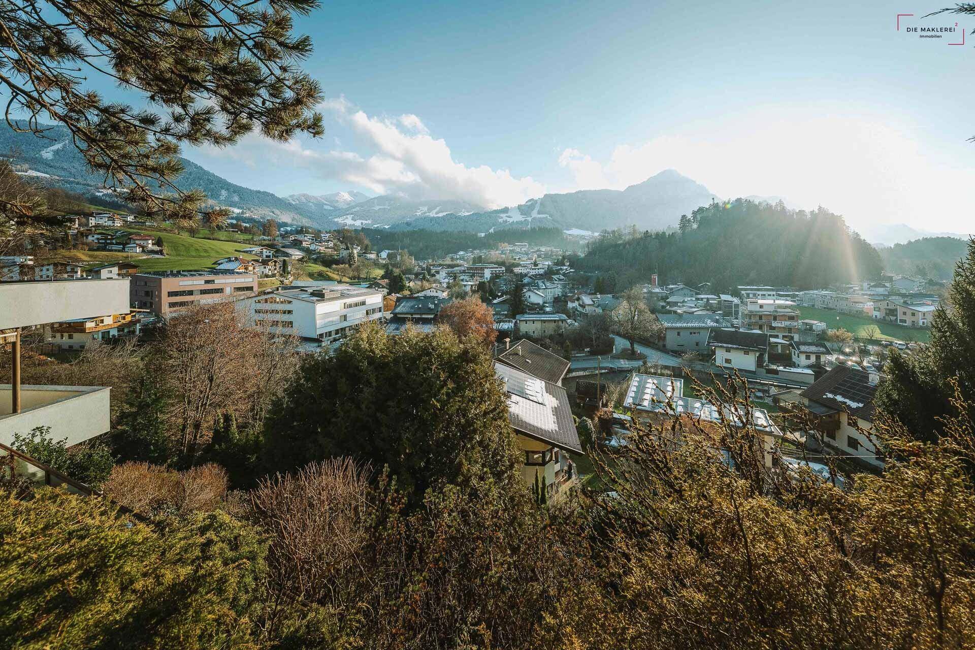 Weite Panoramaaussicht auf die Stadt und die umliegenden schneebedeckten Berge unter blauem Himmel.