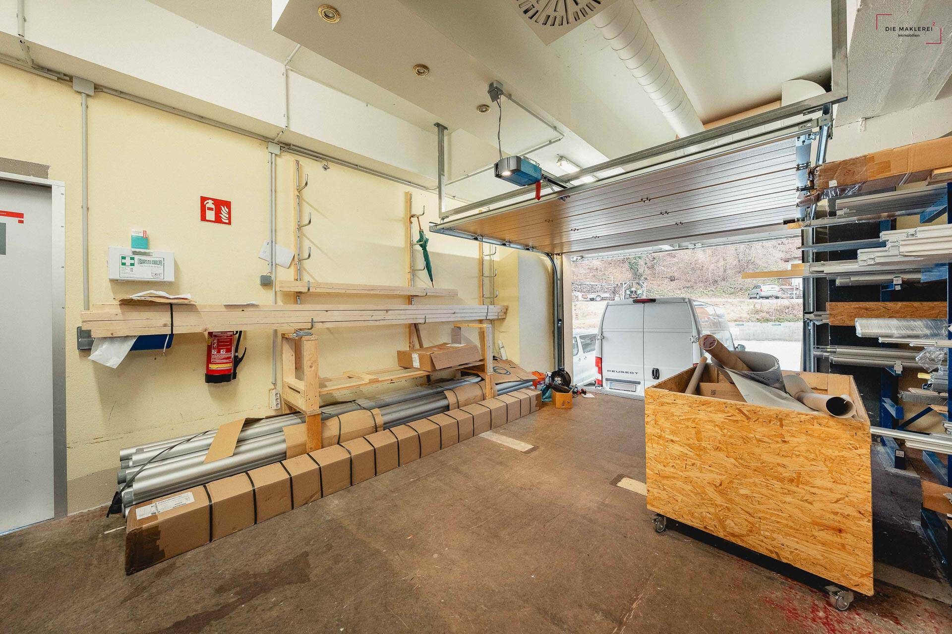 Garagenbereich mit Rolltor, Betonboden und Lagerregalen, geeignet für Fahrzeuge und Materiallagerung.