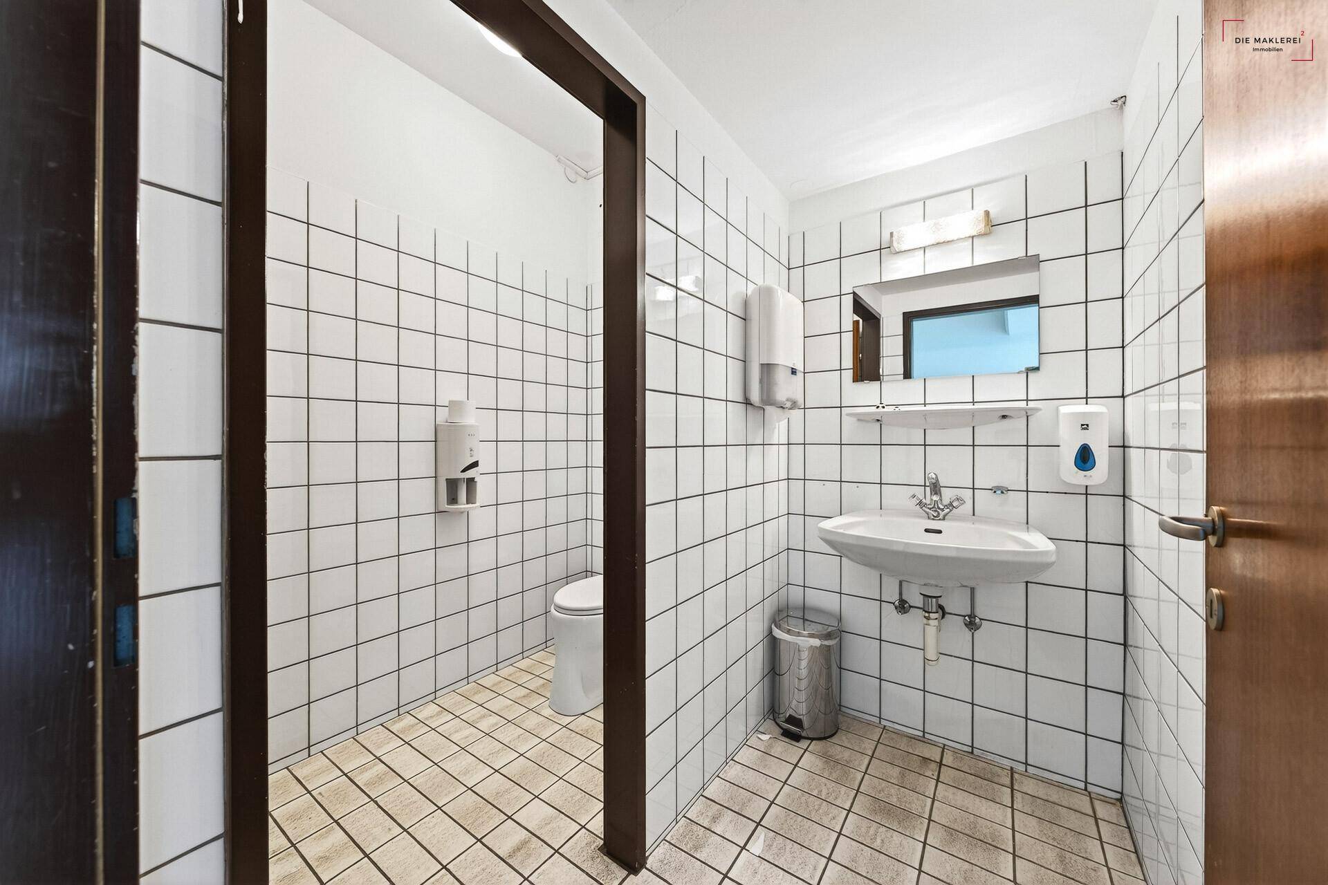 Sauberer Toilettenraum mit weißen Fliesen an Wänden und Boden, ausgestattet mit Waschbecken und WC.