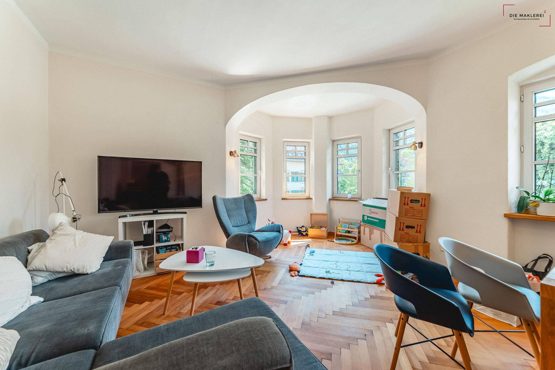 Helles Wohnzimmer mit modernem Mobiliar, Fischgrätparkett und einem gemütlichen Erkerbereich.