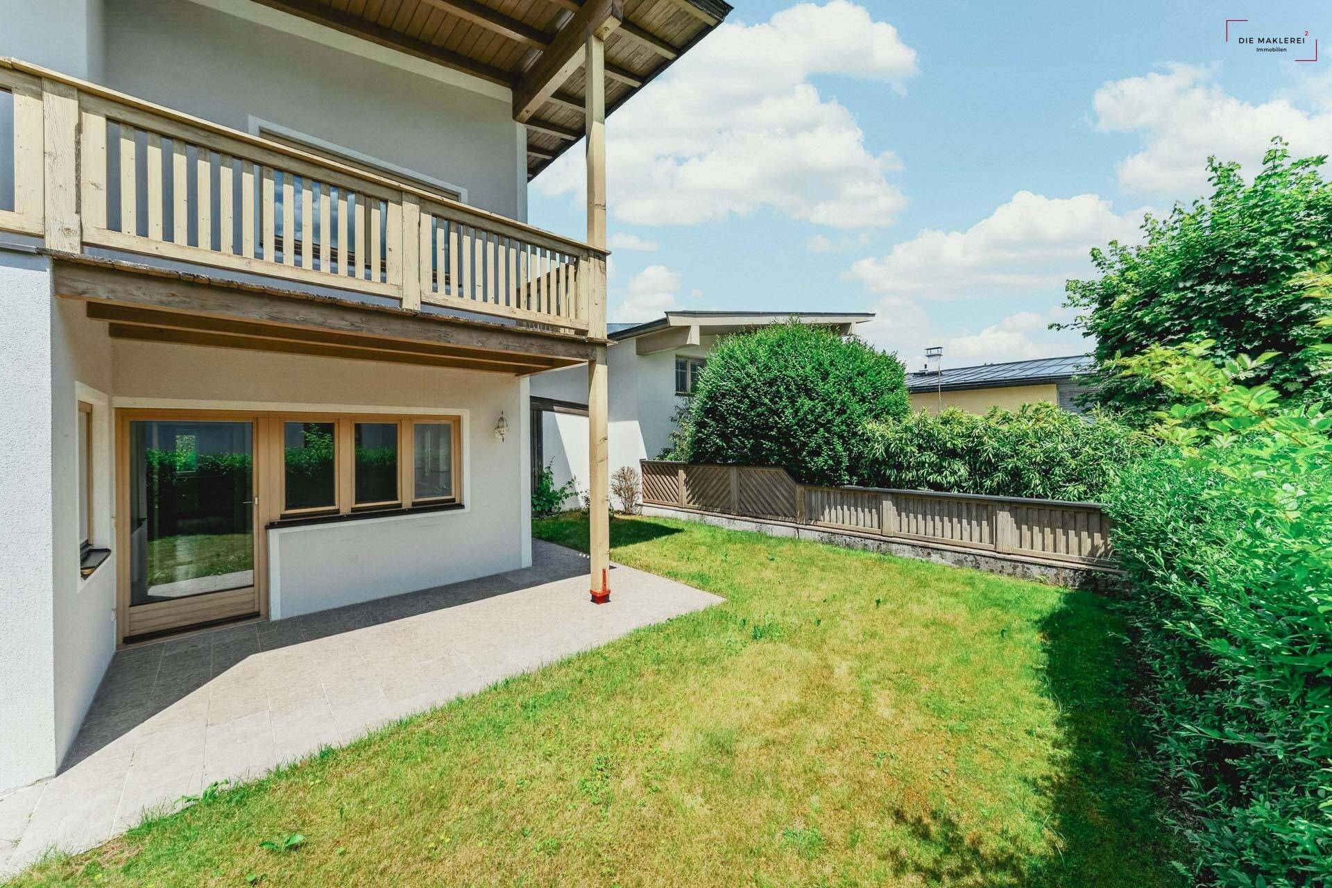 Grüner Gartenbereich mit Rasenfläche und kleiner Terrasse am Haus.