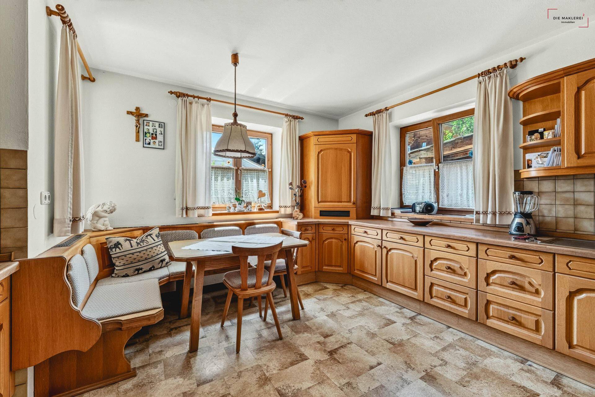 Gemütliche Wohnküche im Landhausstil mit Holzeinbauten, Essecke und Fenstern mit Vorhängen.