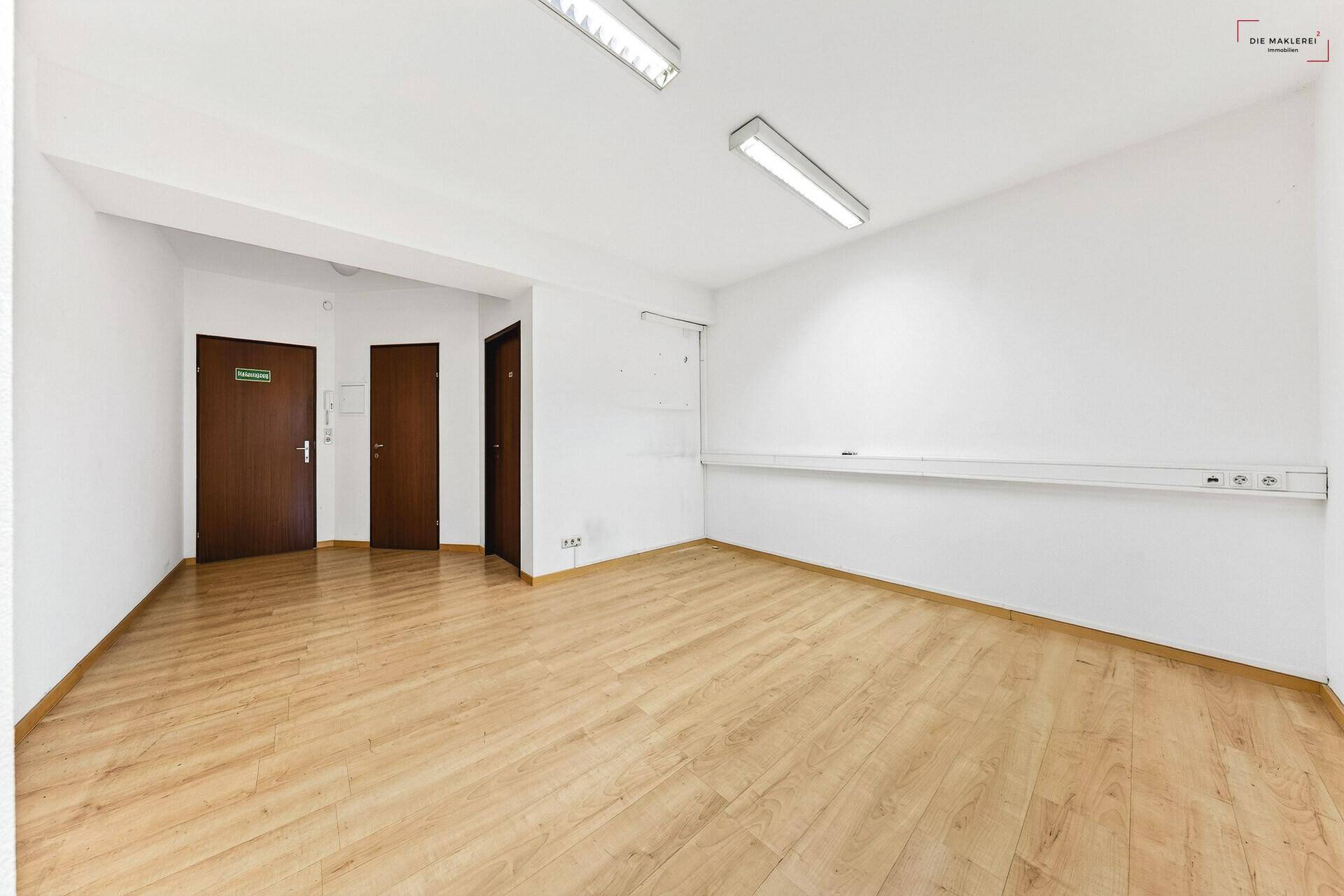 Leerer Büroraum mit hellem Laminatboden, weißen Wänden und mehreren Türen, bereit zur individuellen Gestaltung.