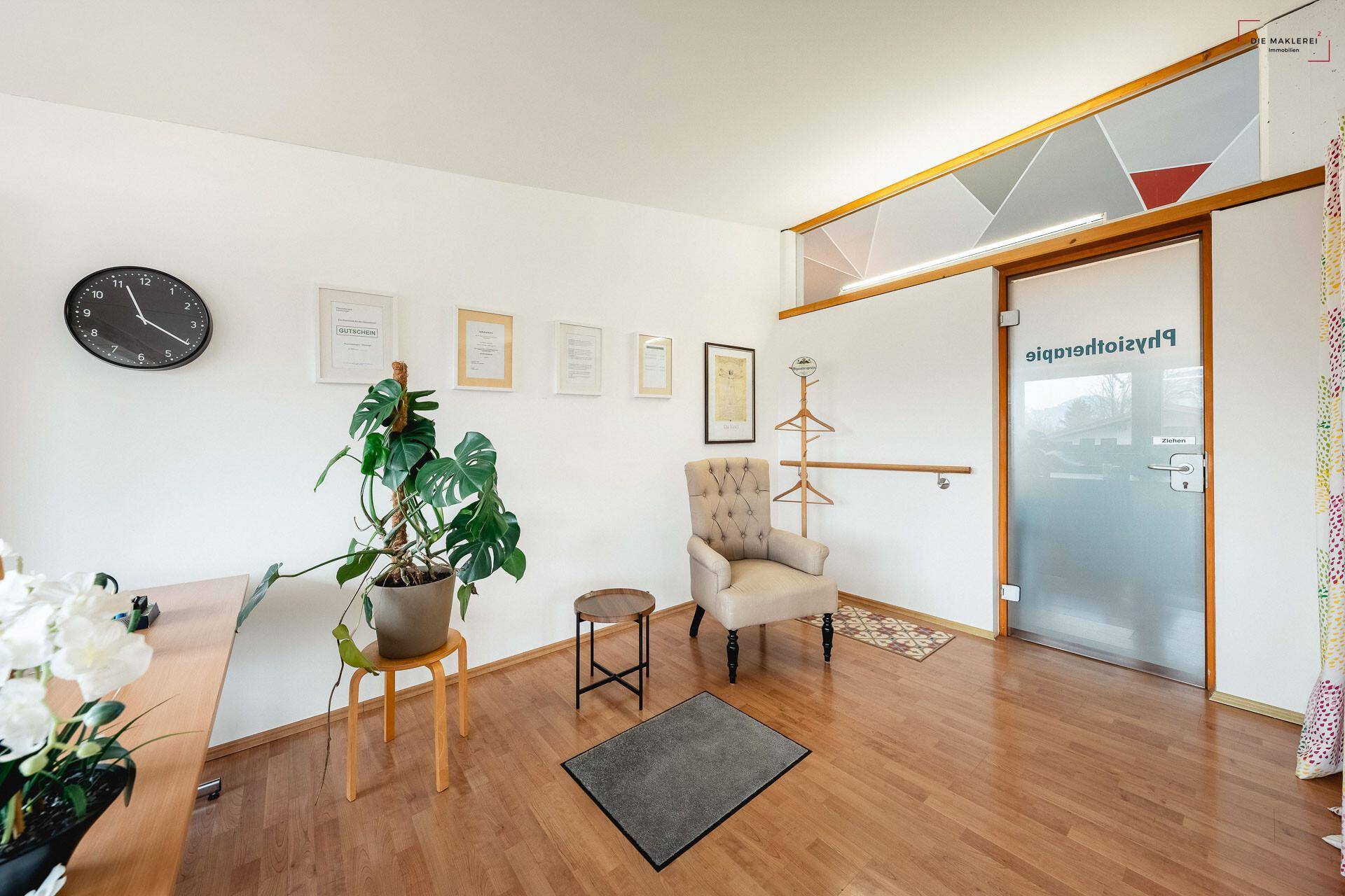 Heller Wartebereich mit Holzboden, bequemen Sessel und Milchglastür zur Physiotherapie.